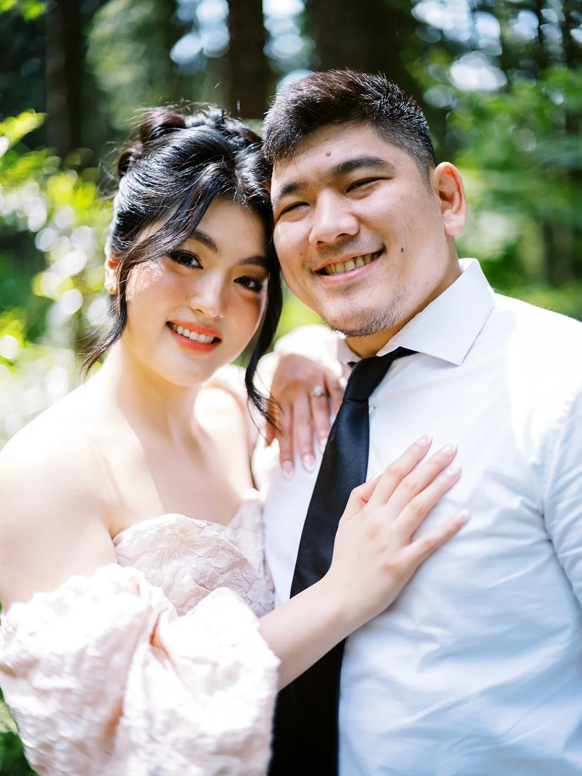 Close portrait of a couple embracing outdoors, bride in an off-shoulder dress and groom in white shirt and black tie.