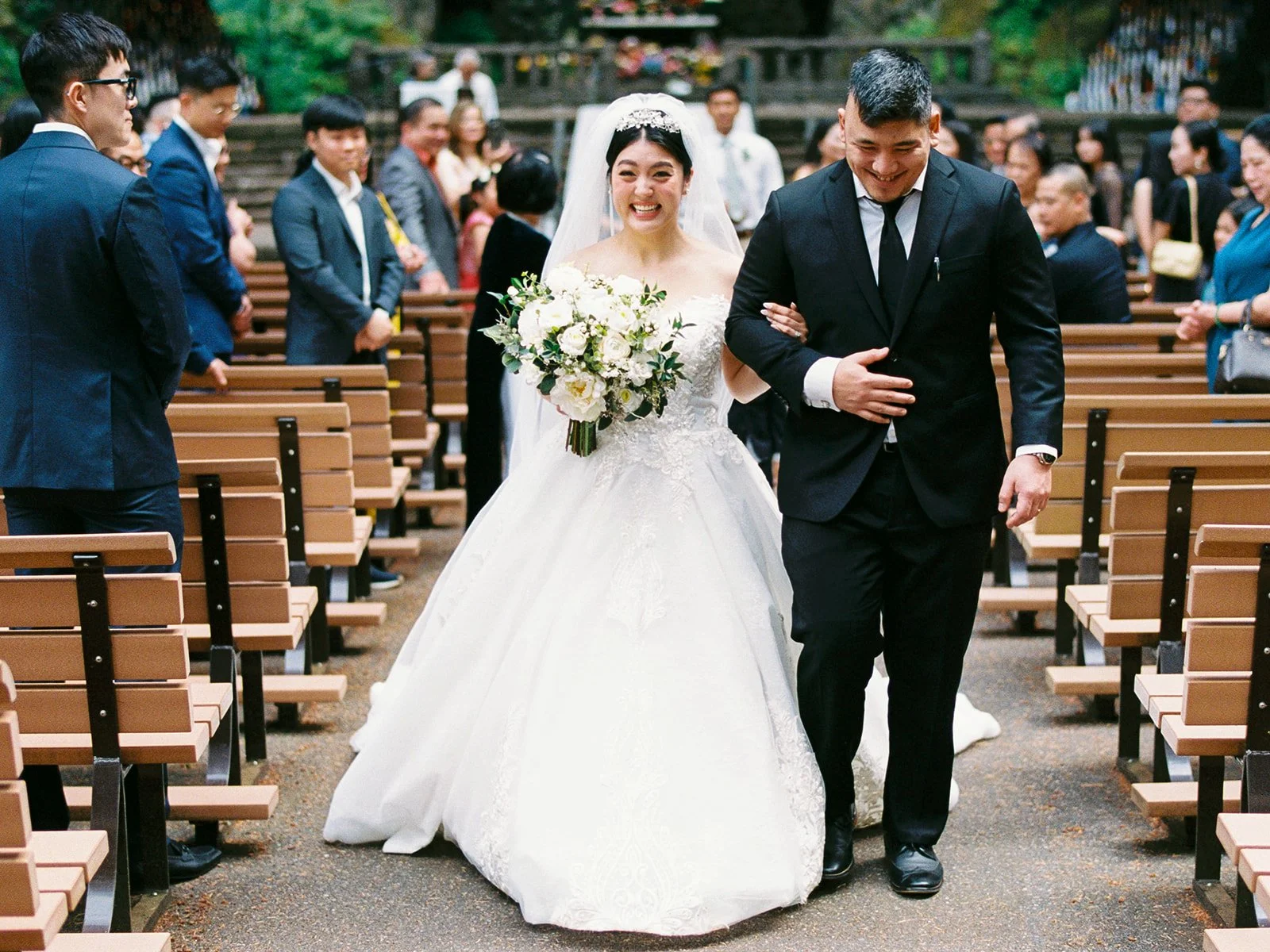 Bride and groom walking down the aisle together between rows of wooden benches after the ceremony.