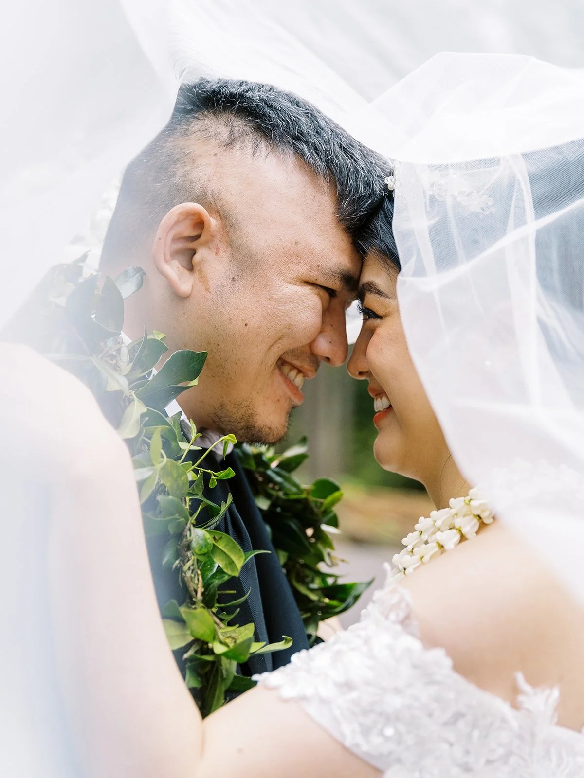 Bride and groom touching foreheads and smiling under the bride’s veil during outdoor portraits.