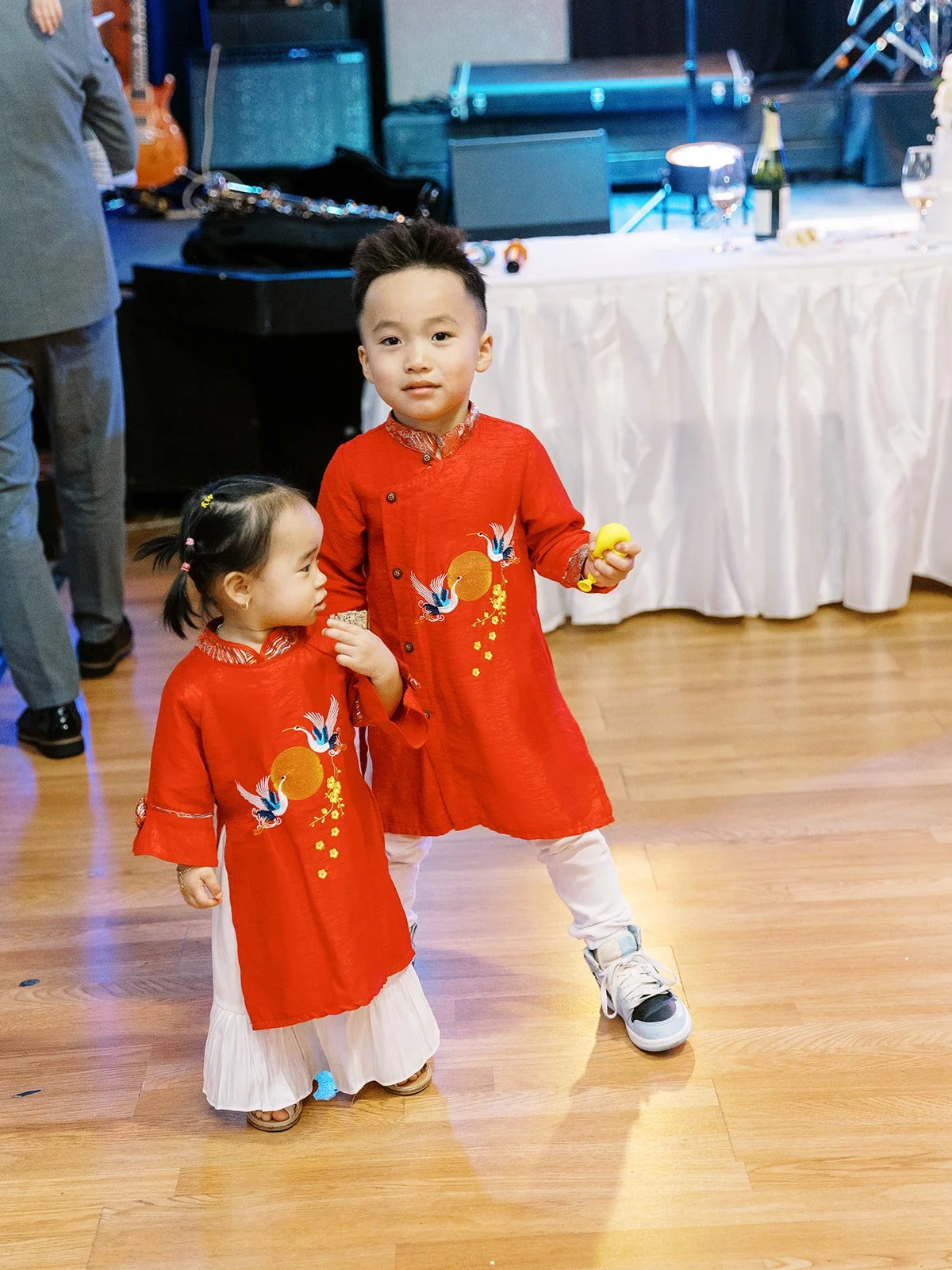 Two children wearing red traditional Vietnamese áo dài outfits standing together at the wedding reception.