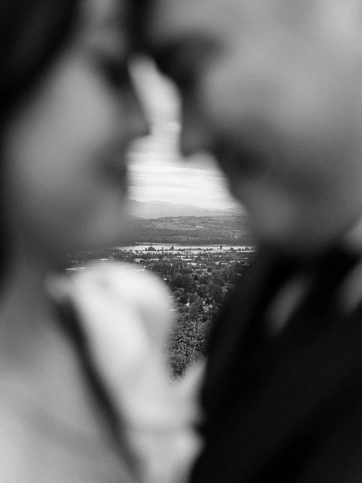 Black and white photo of a scenic river and mountain view framed between two blurred figures.