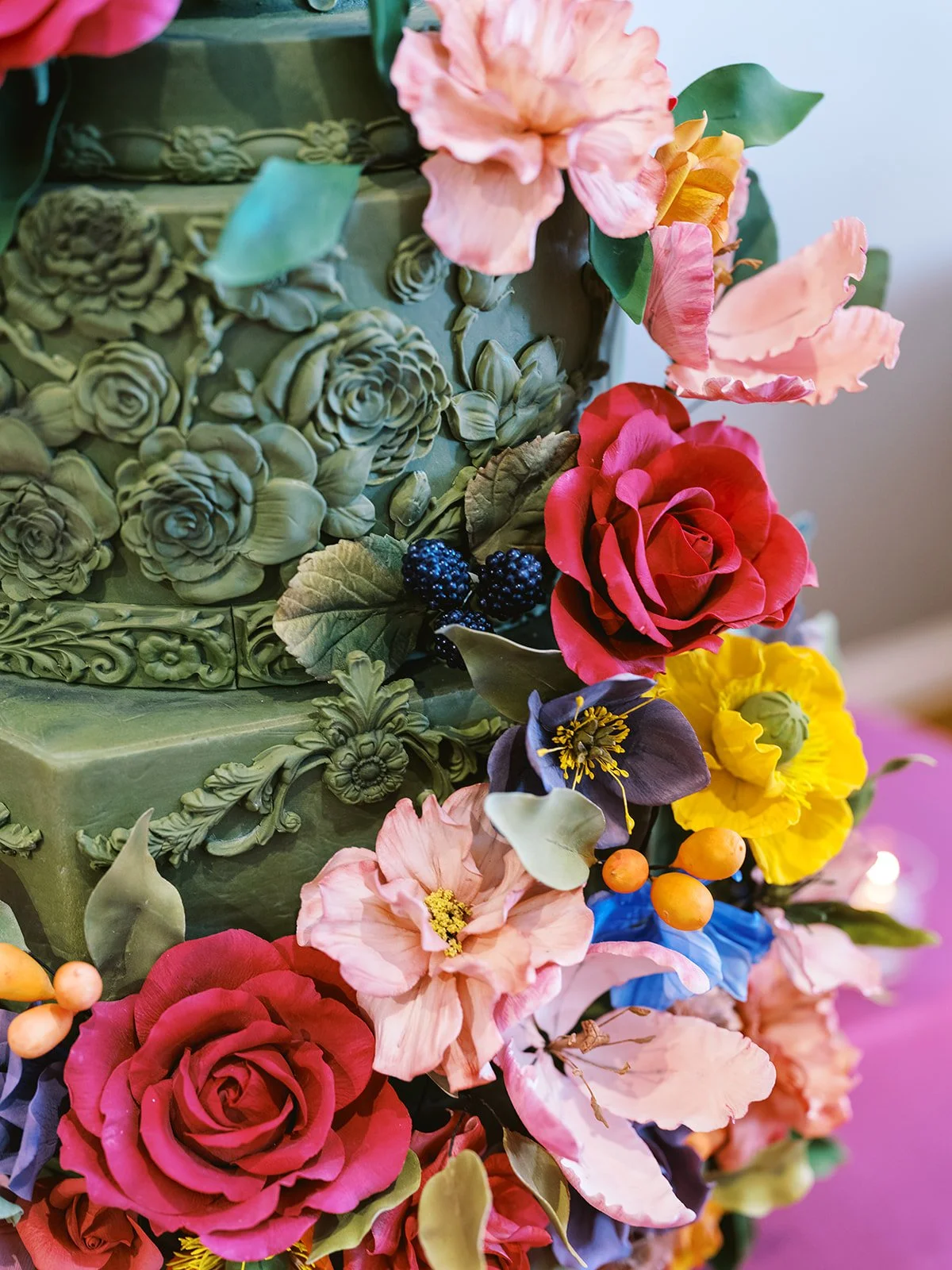 Close-up of colorful sugar flowers and detailed green icing on ornate multi-tier wedding cake.