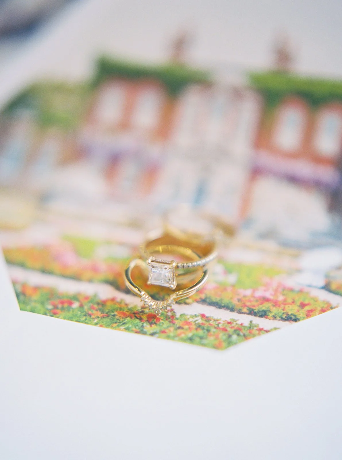 Gold engagement ring and wedding band resting on illustrated envelope liner with garden scene.