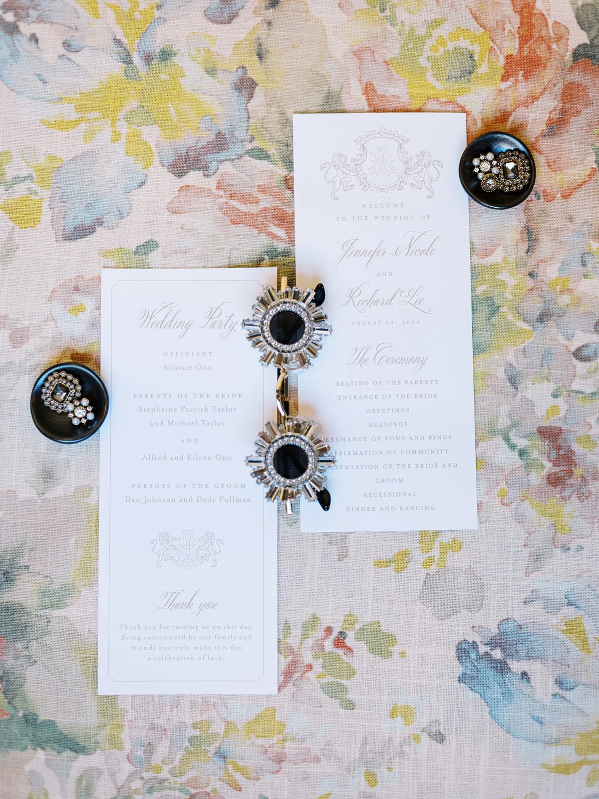 Wedding ceremony programs with decorative brooches arranged on pastel floral fabric.