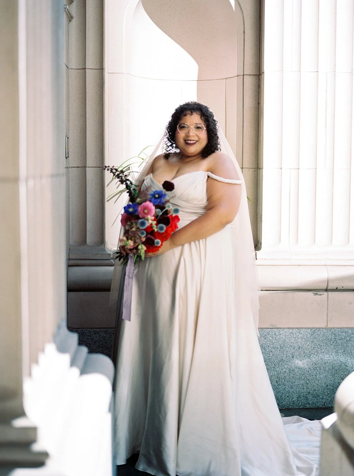 Bride standing between stone columns holding bouquet during wedding portraits.