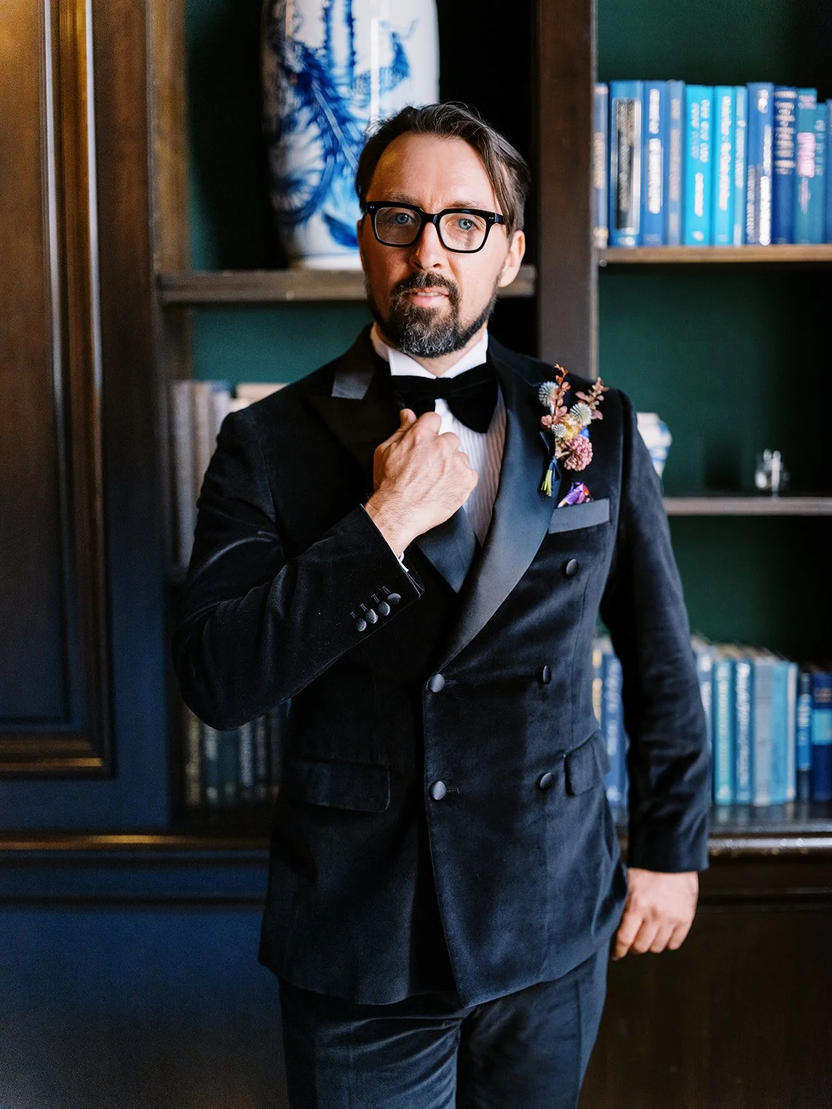 Groom in tuxedo standing in front of bookshelves in historic hotel library.