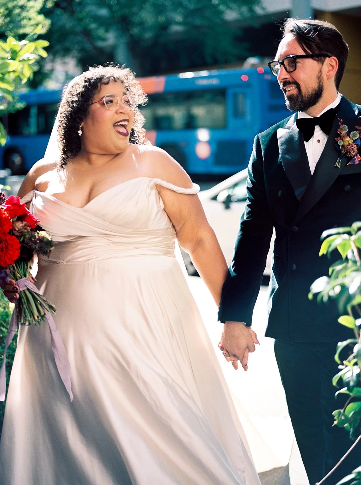 Bride and groom walking hand in hand down city sidewalk after first look portraits.