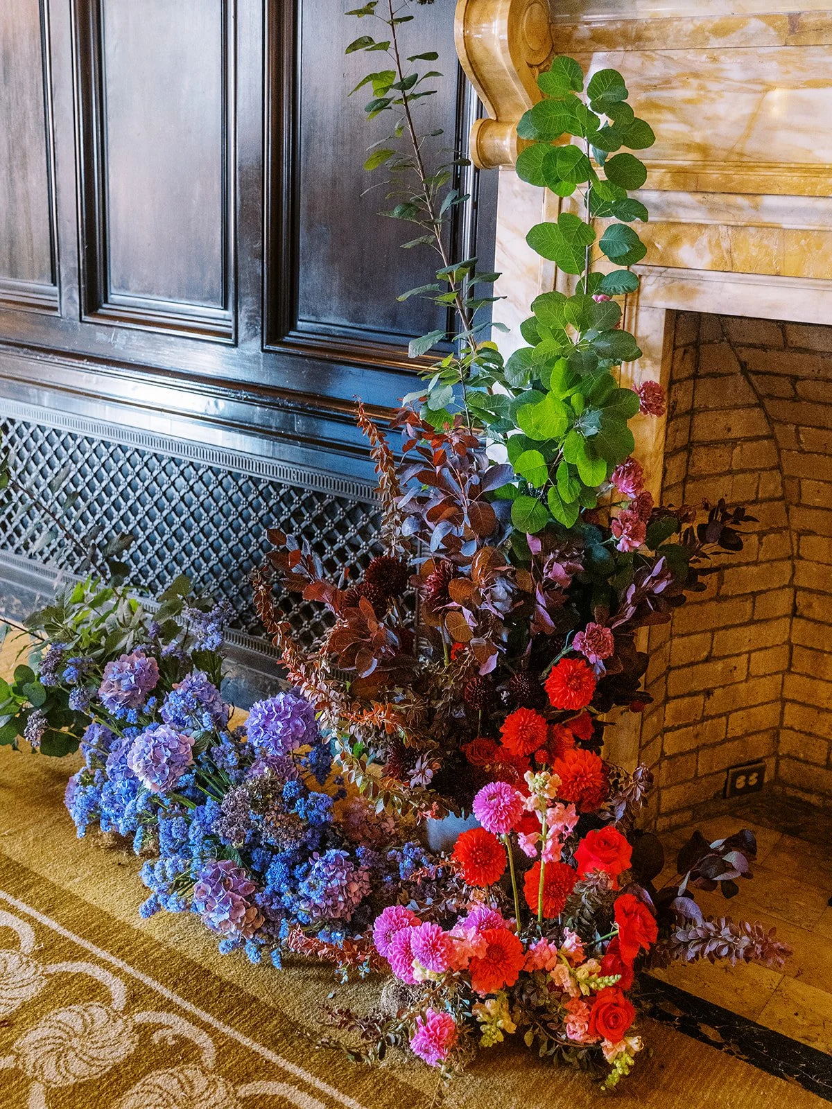 Large ceremony floral installation beside marble fireplace in historic hotel library.