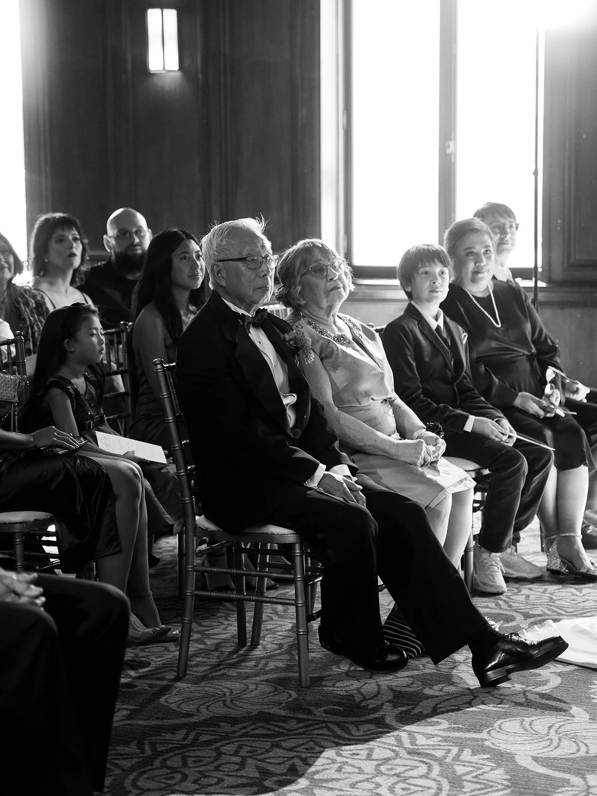 Wedding guests seated and watching ceremony in softly lit library space.
