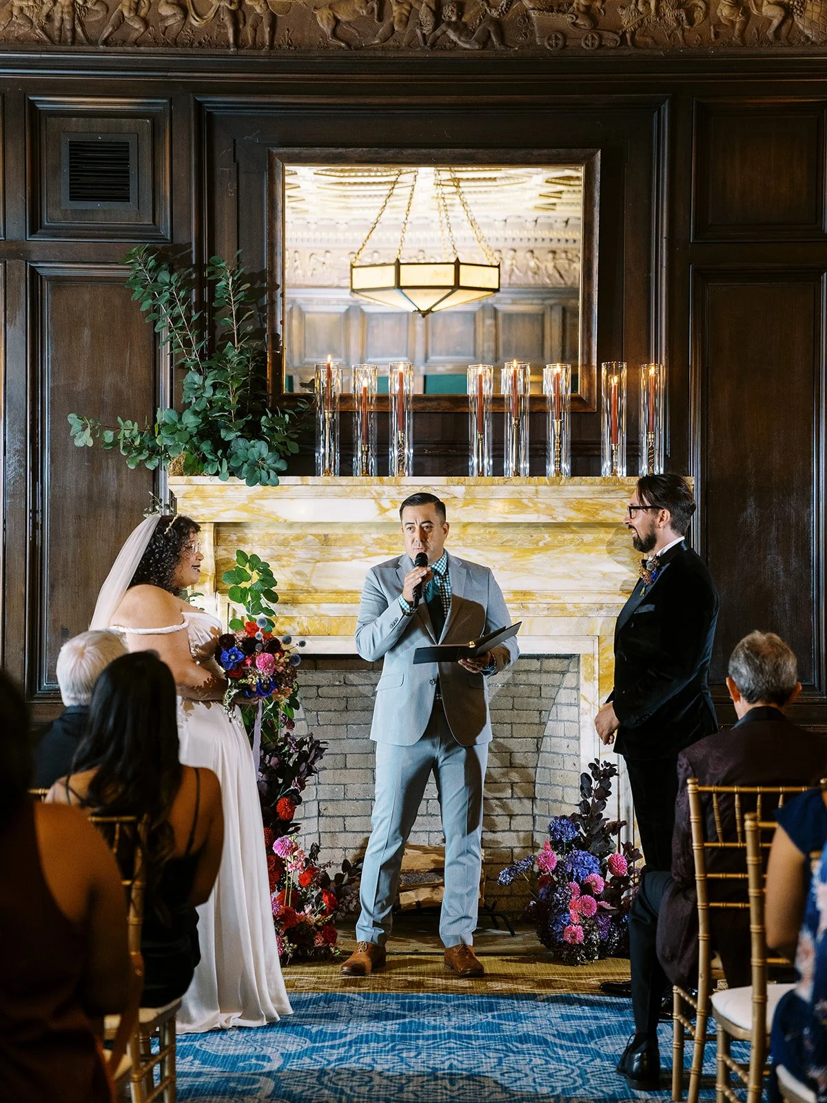 Officiant speaking during wedding ceremony while couple stands together in front of marble fireplace.