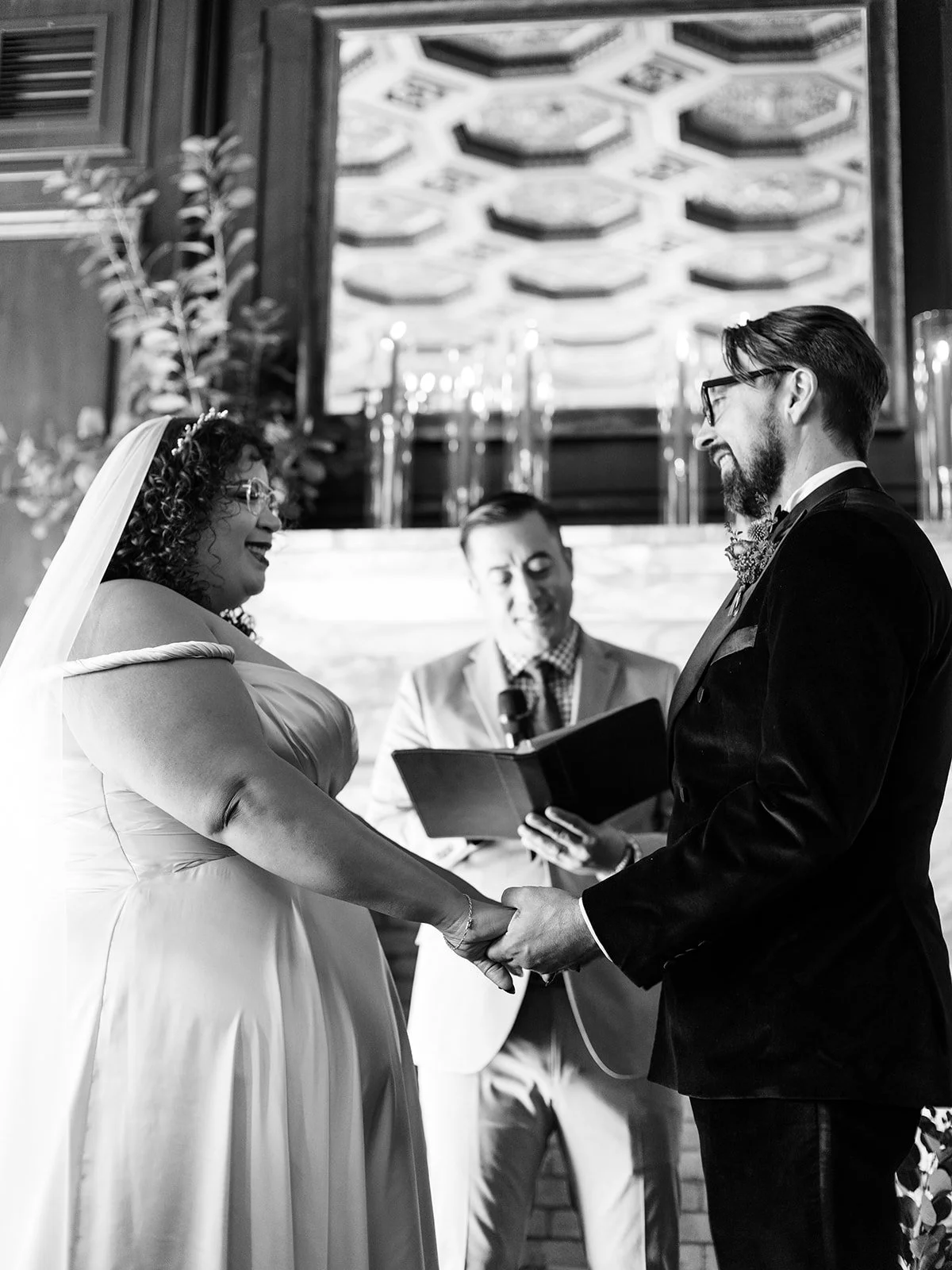Officiant reading during ceremony while bride and groom stand in front of fireplace with floral arrangements.
