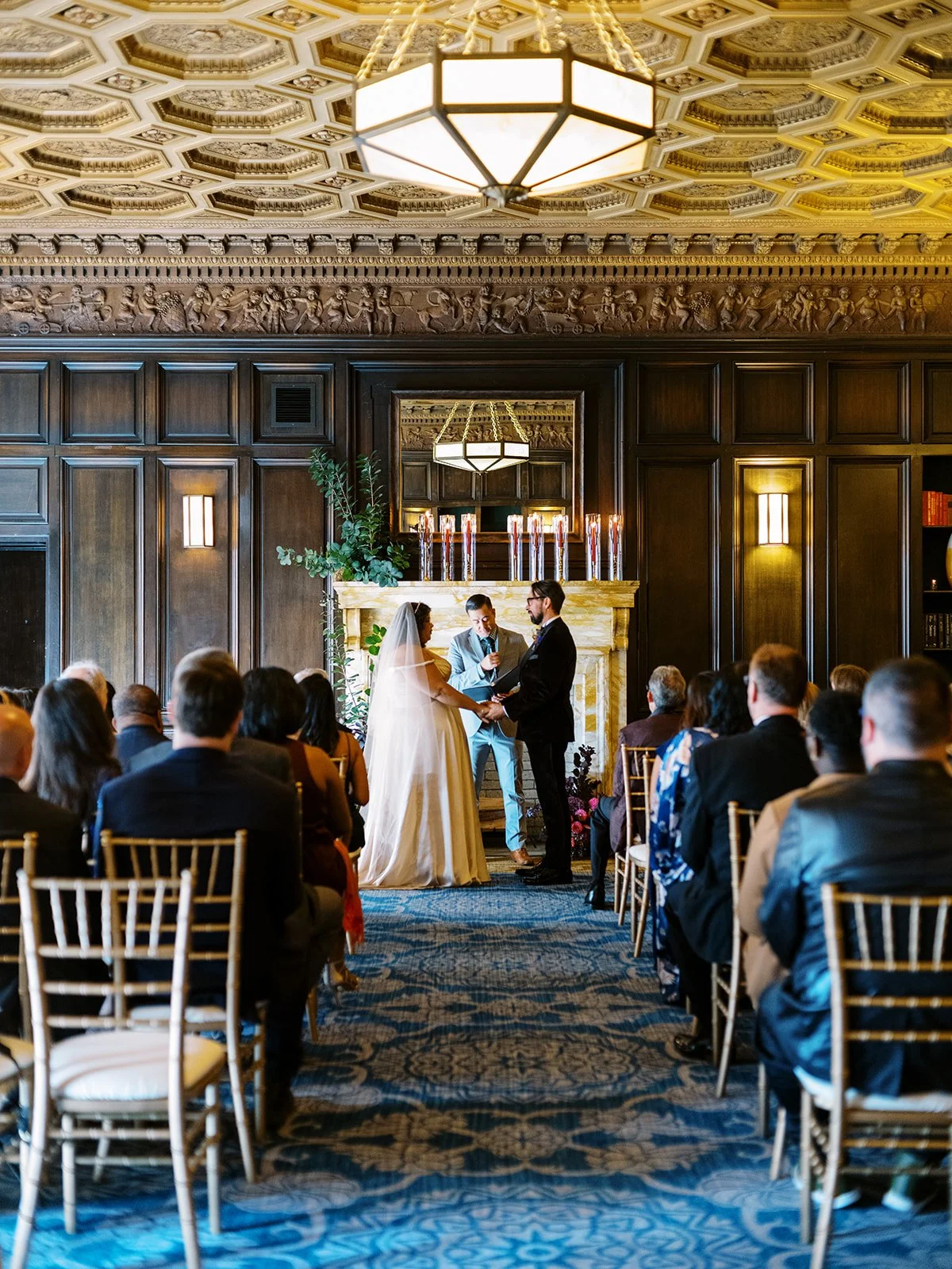 Bride and groom holding hands during wedding ceremony as officiant reads from vow book.