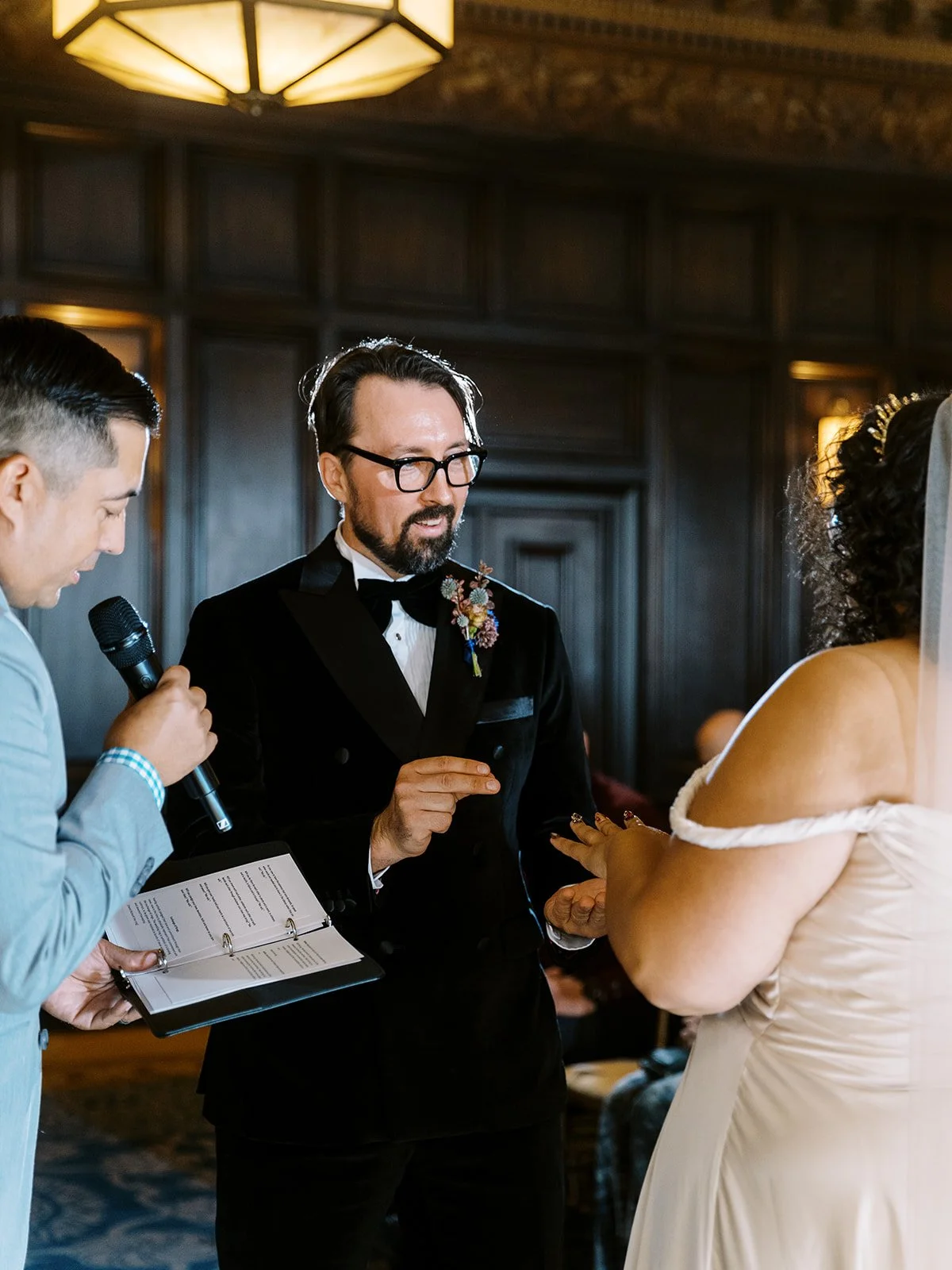 Groom placing wedding ring on bride’s finger during indoor ceremony.