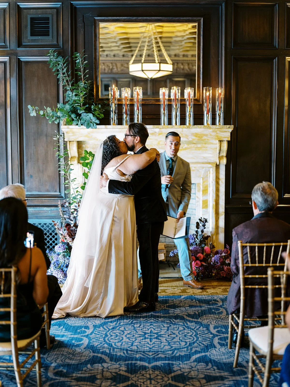 Newly married couple sharing first kiss during ceremony in historic hotel library.