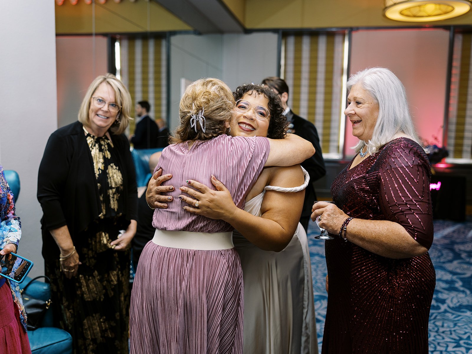 Bride hugging guest during reception while other guests watch and smile.