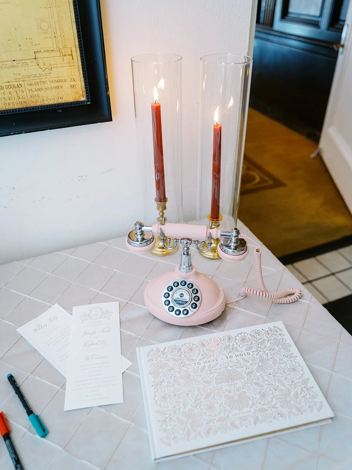 Vintage pink rotary phone guestbook with candles and wedding programs on reception table.