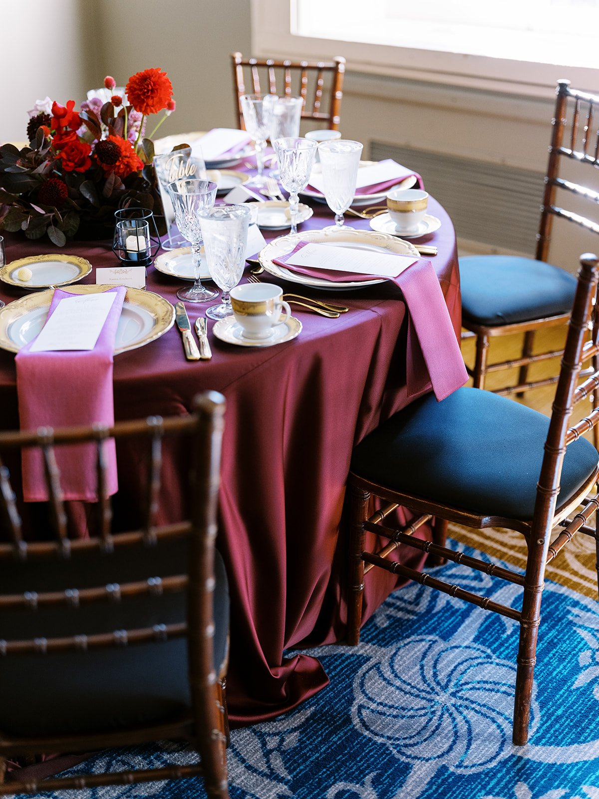 Reception table with burgundy linens, gold-rimmed plates, and crystal glassware.