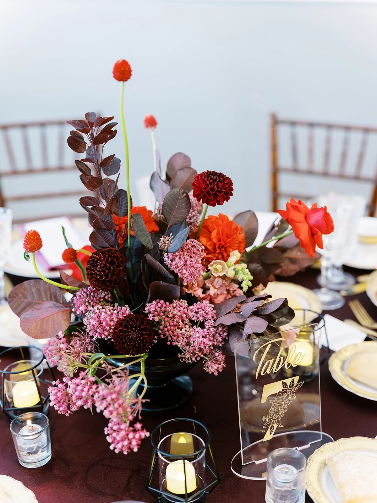 Colorful floral centerpiece with dahlias and pink blooms beside acrylic “Table 7” sign on reception table.