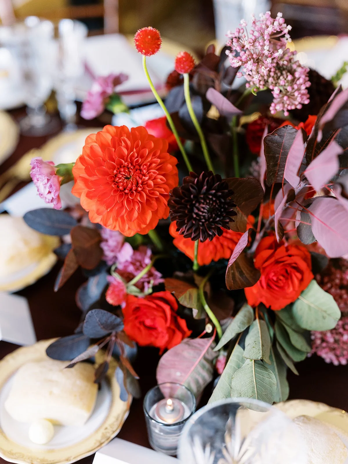 Close-up of vibrant red and dark dahlia flowers in reception table centerpiece with candles and place settings.