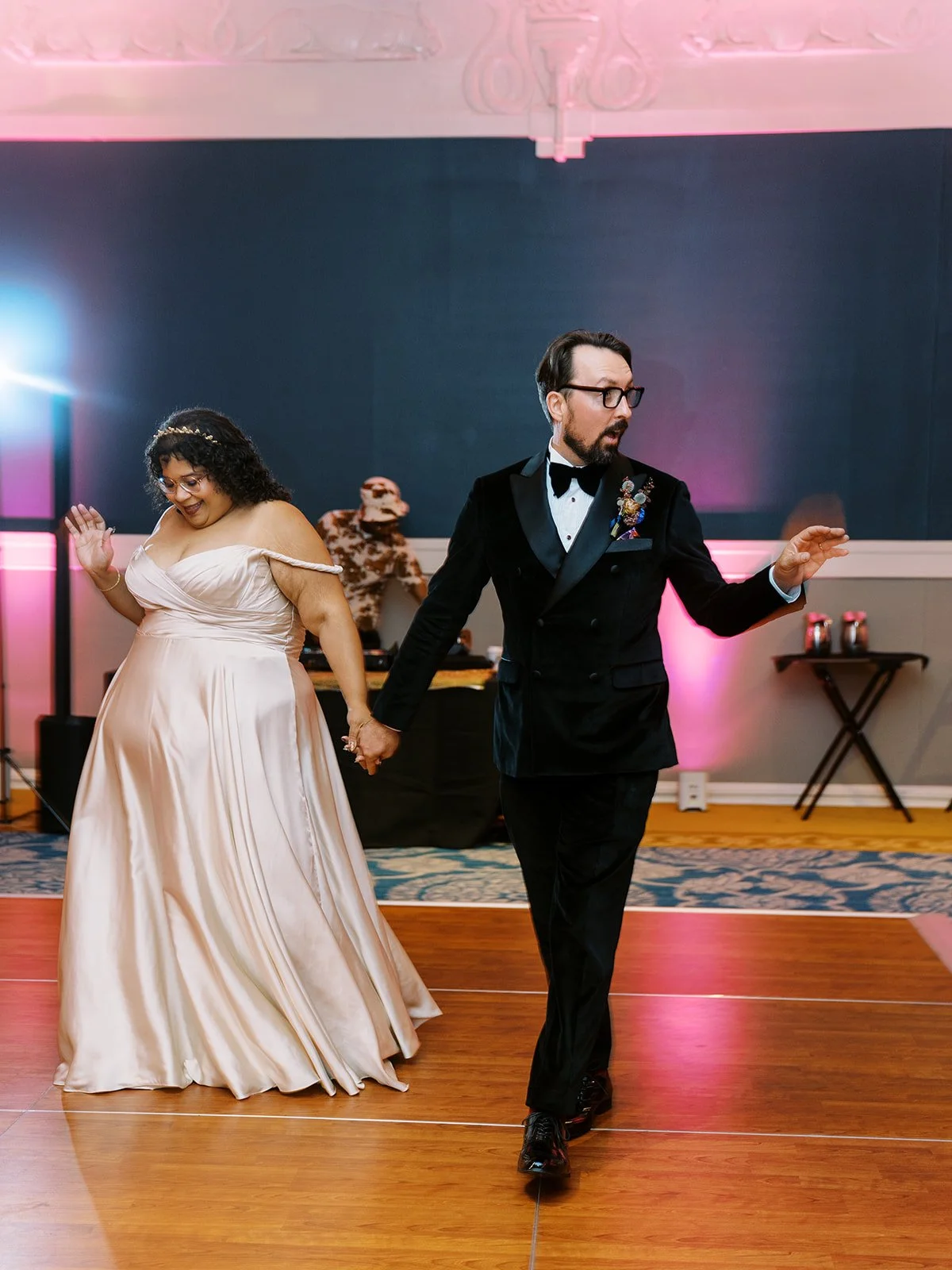 Bride and groom holding hands while entering reception dance floor for first dance.