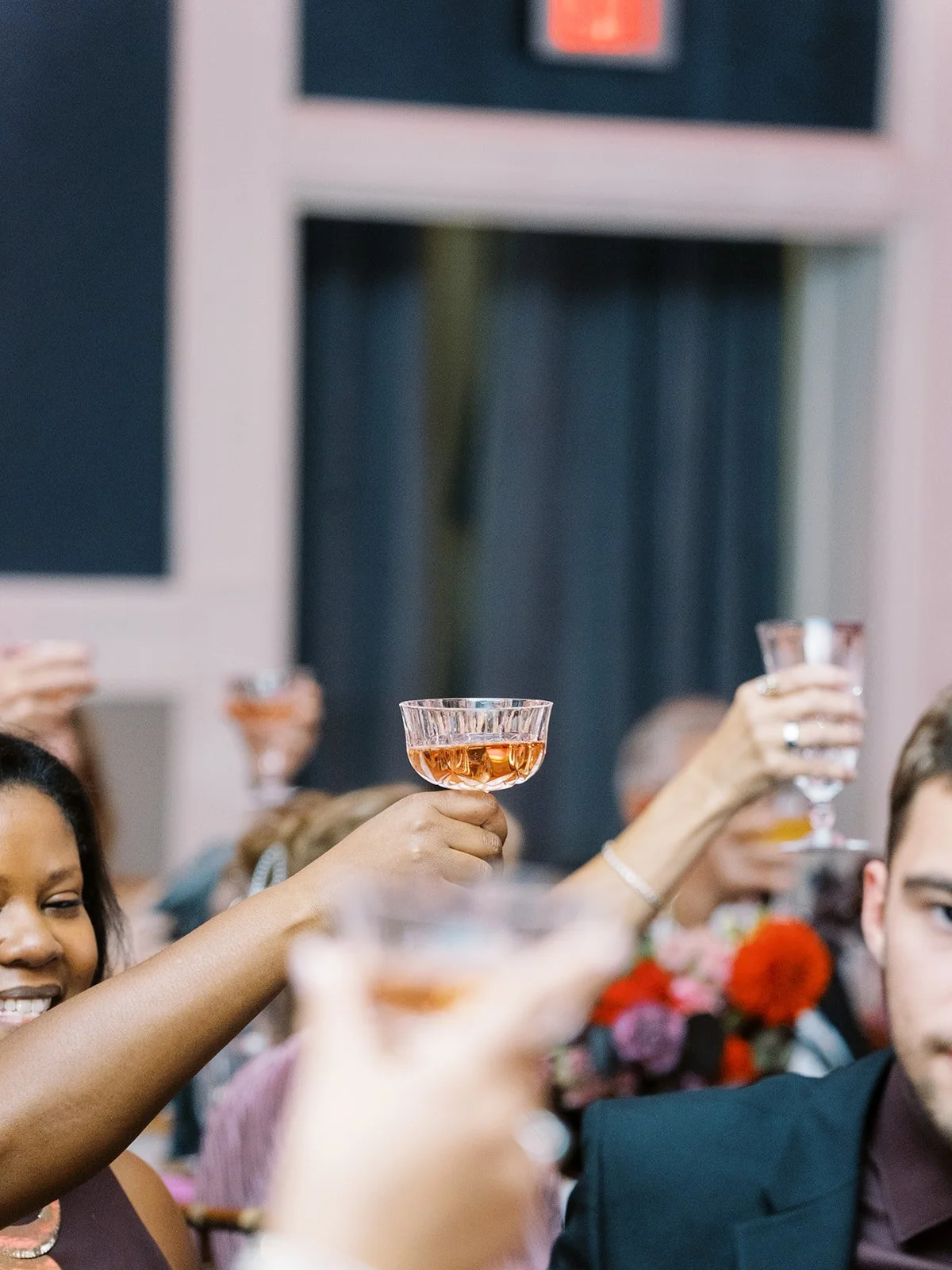 Guests raising coupe glasses during champagne toast at wedding reception.