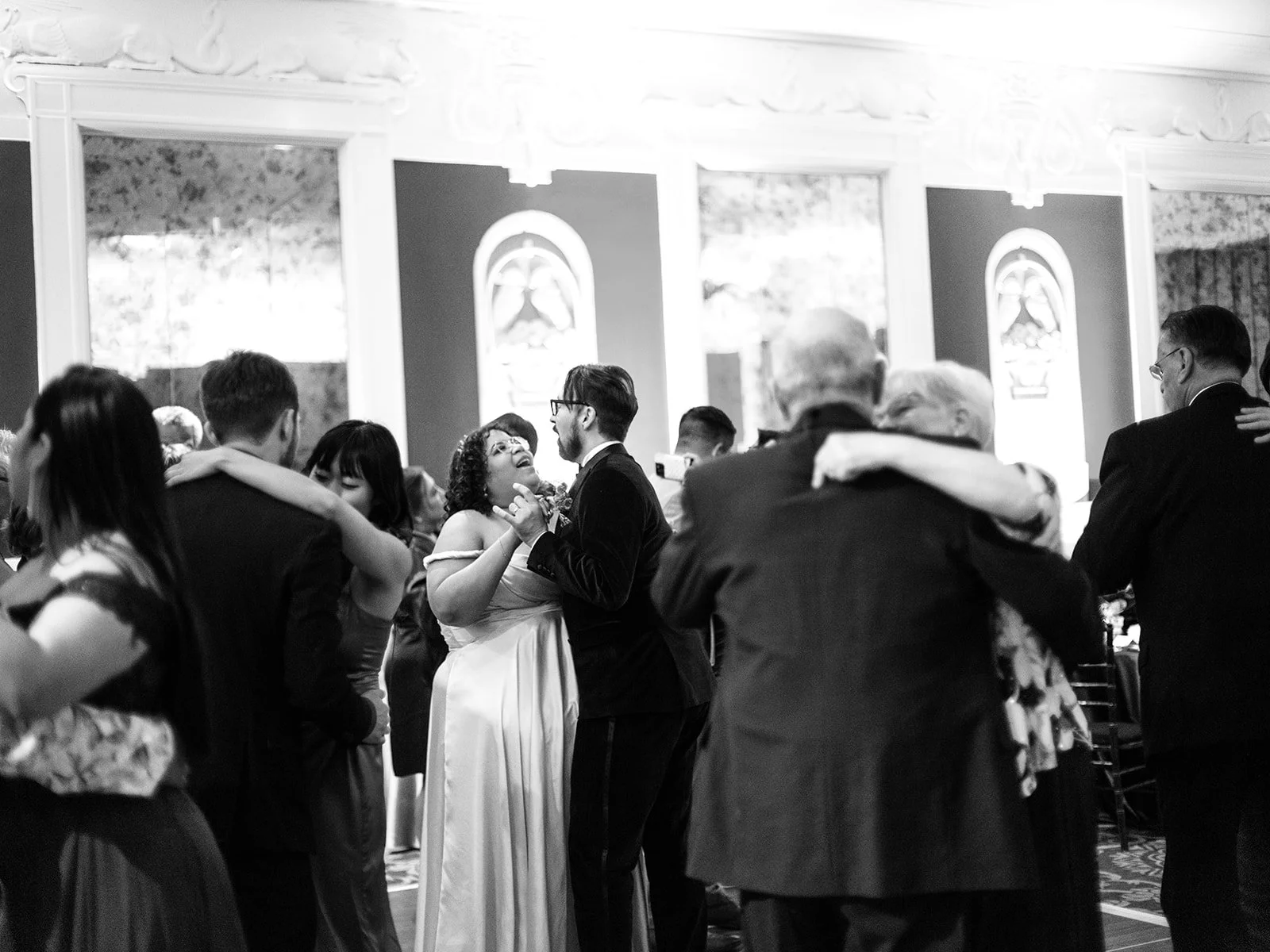 Black and white photo of the bride and groom dancing together surrounded by other couples on a full dance floor