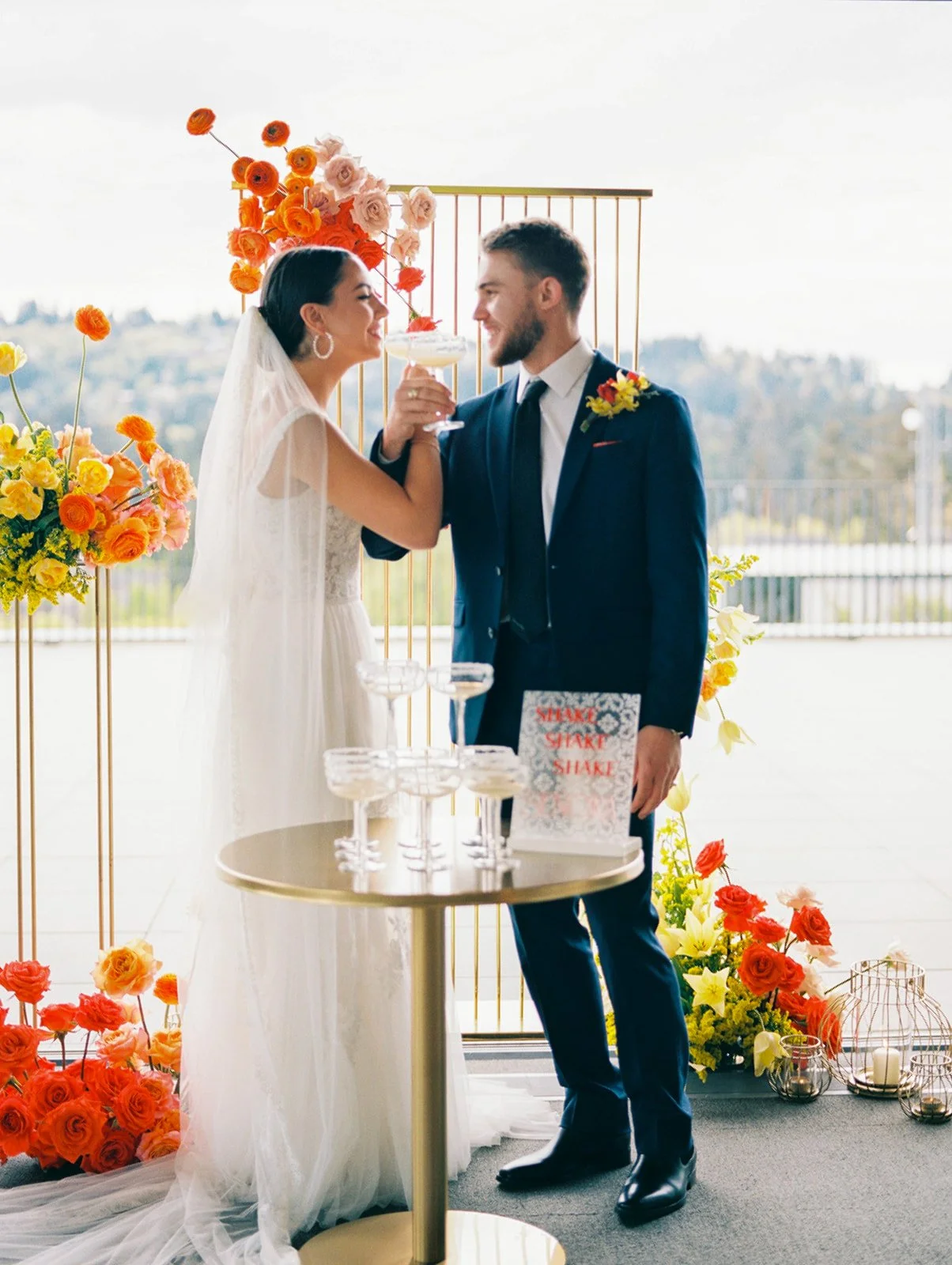 Bride and groom toasting with coupe glasses beside margarita tower and bright floral decor at Ironlight wedding