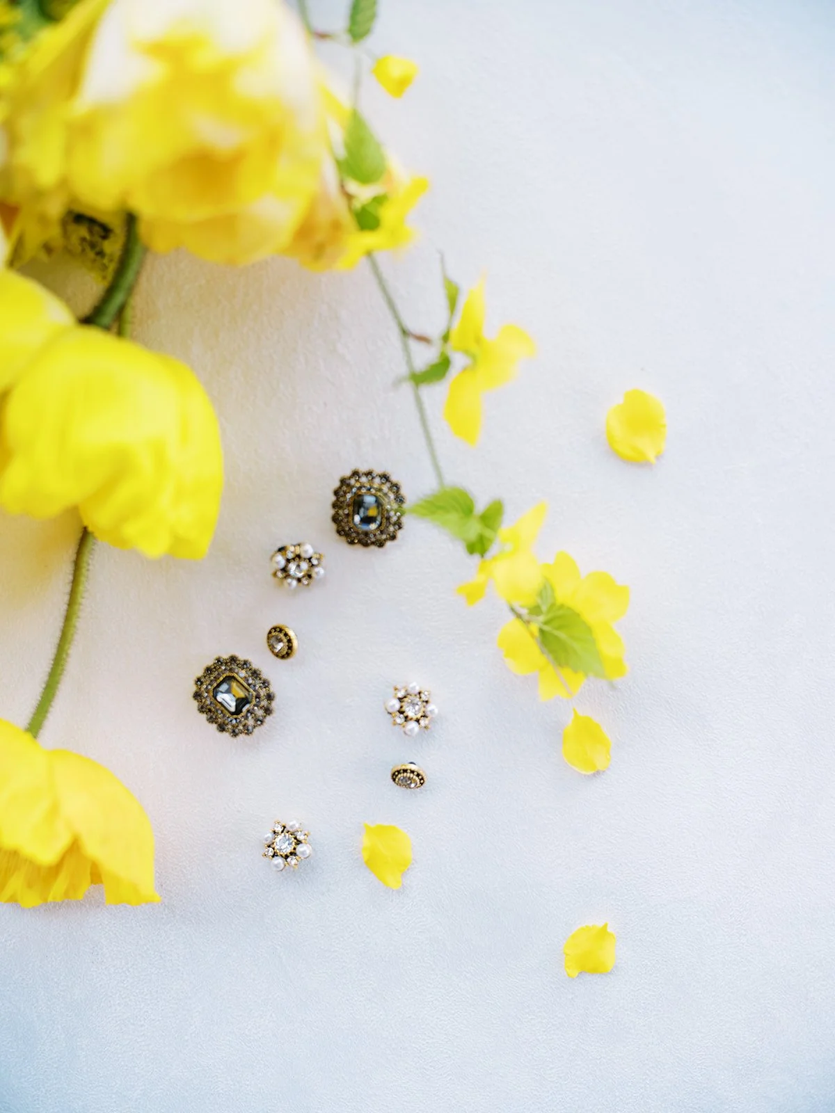 Vintage-style earrings and rings styled with yellow flowers on light background for Portland wedding detail photo