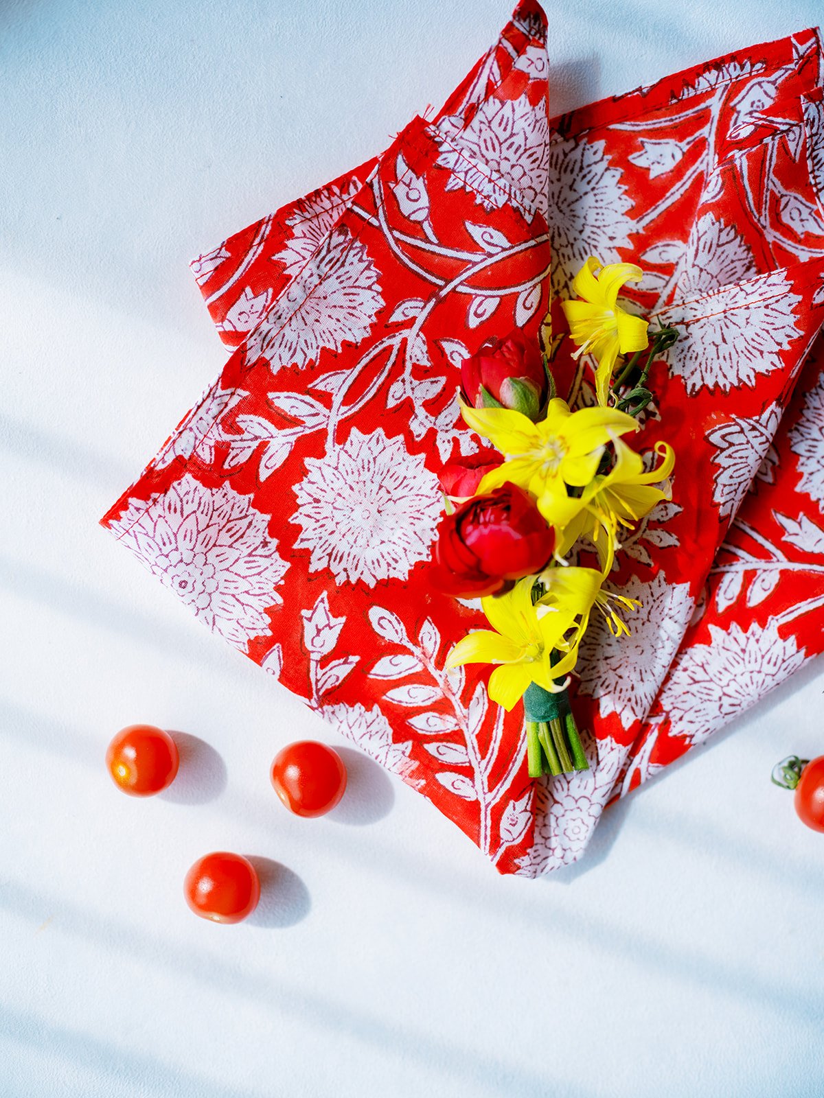 Red patterned napkin with yellow and red boutonniere styled with cherry tomatoes for Portland wedding details