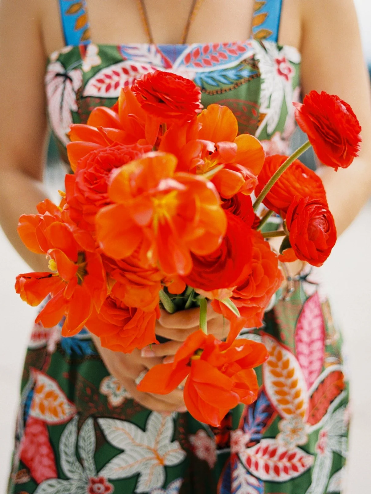 Bridesmaid holding vibrant red and orange bouquet with ranunculus and orchids for Portland wedding