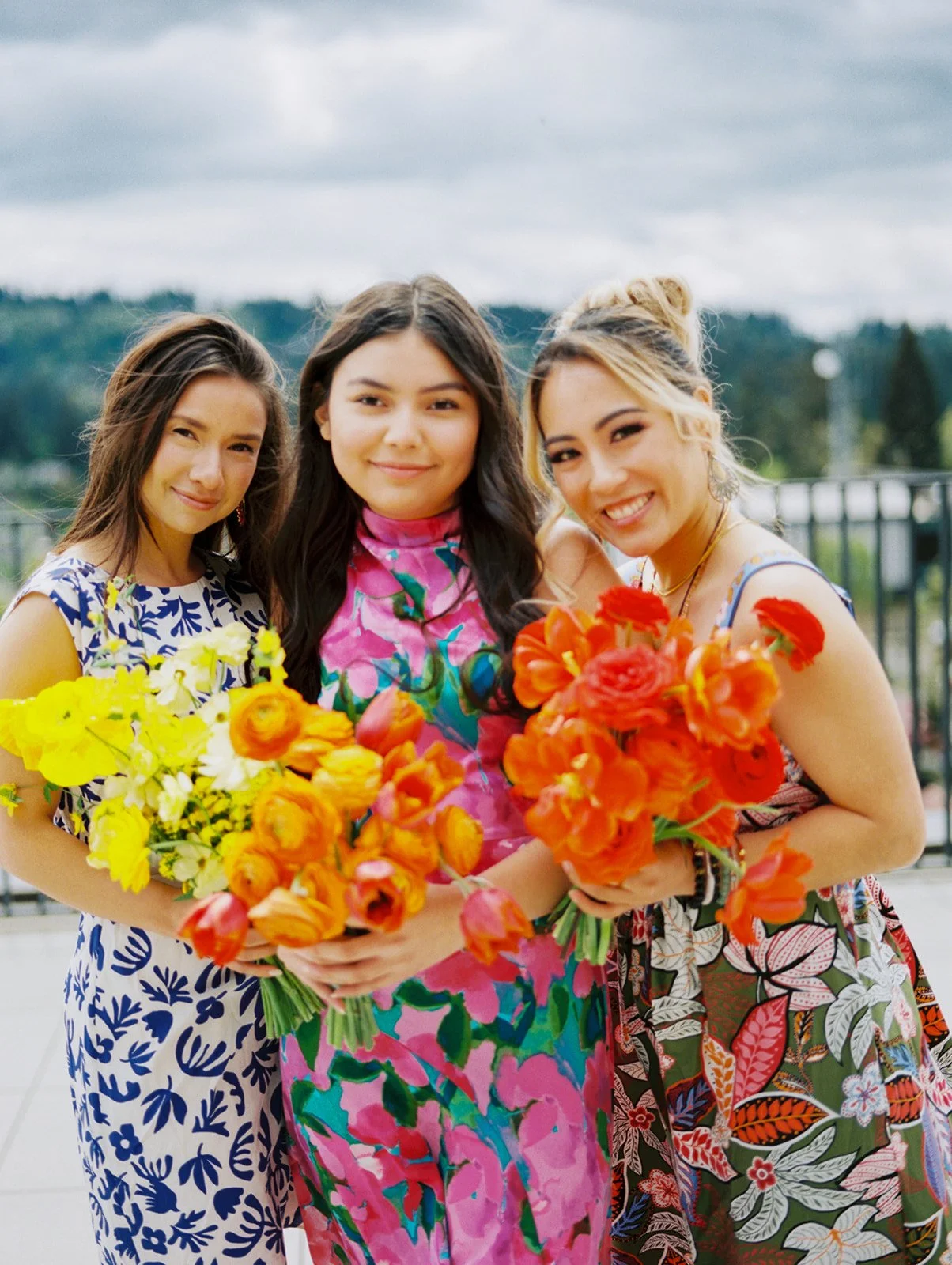 Bridesmaids in patterned dresses with bright florals overlooking Oregon skyline at Ironlight