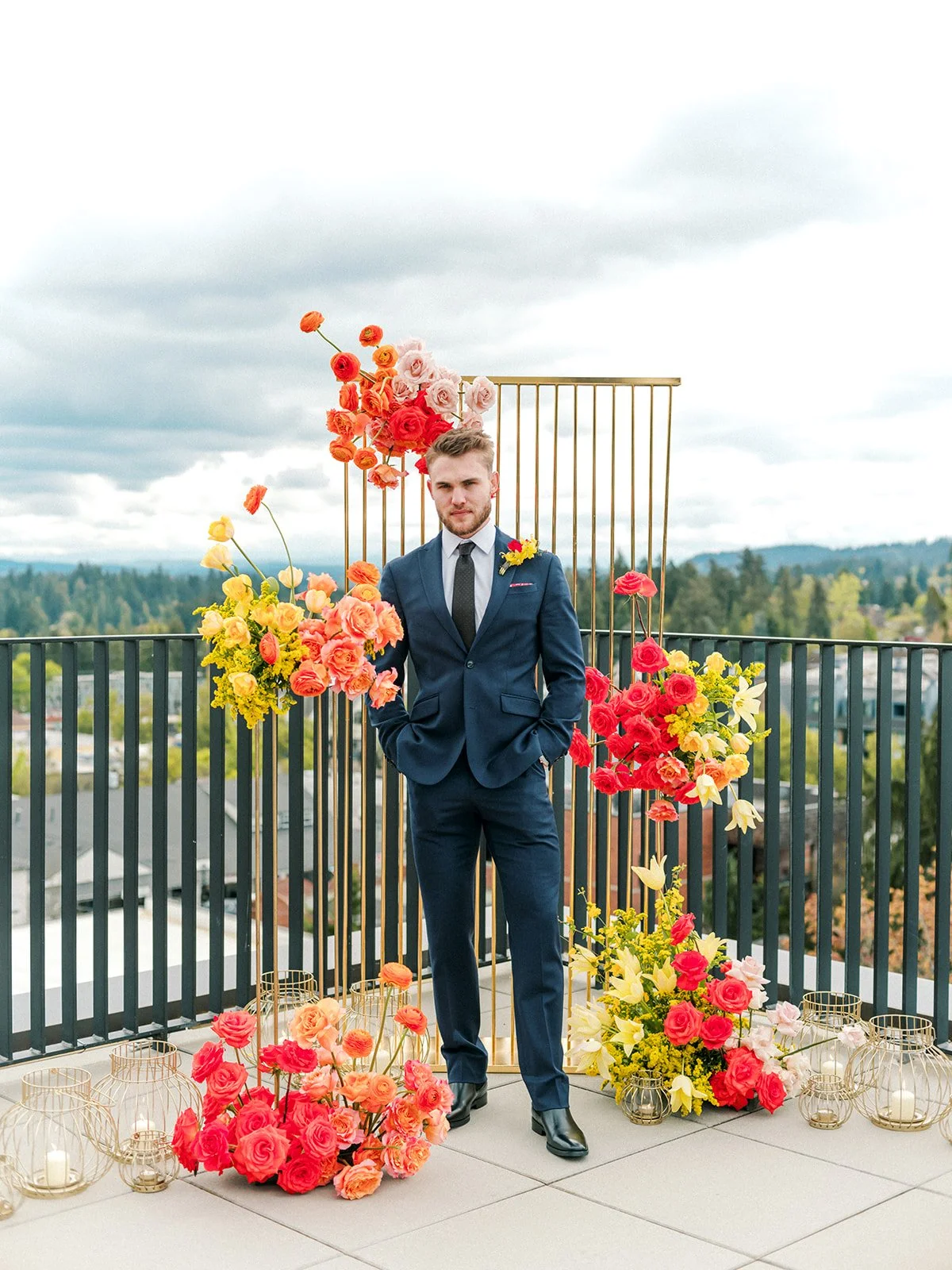 Groom portrait with hands in pockets framed by colorful flowers and modern gold backdrop