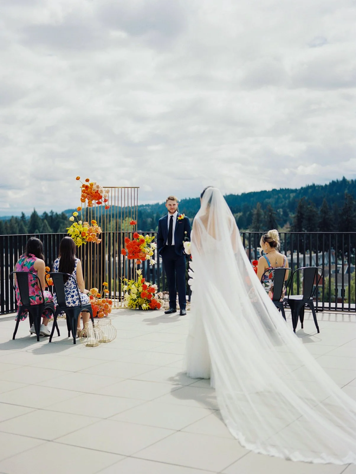Bride walking toward groom during intimate rooftop ceremony with guests seated and floral installations