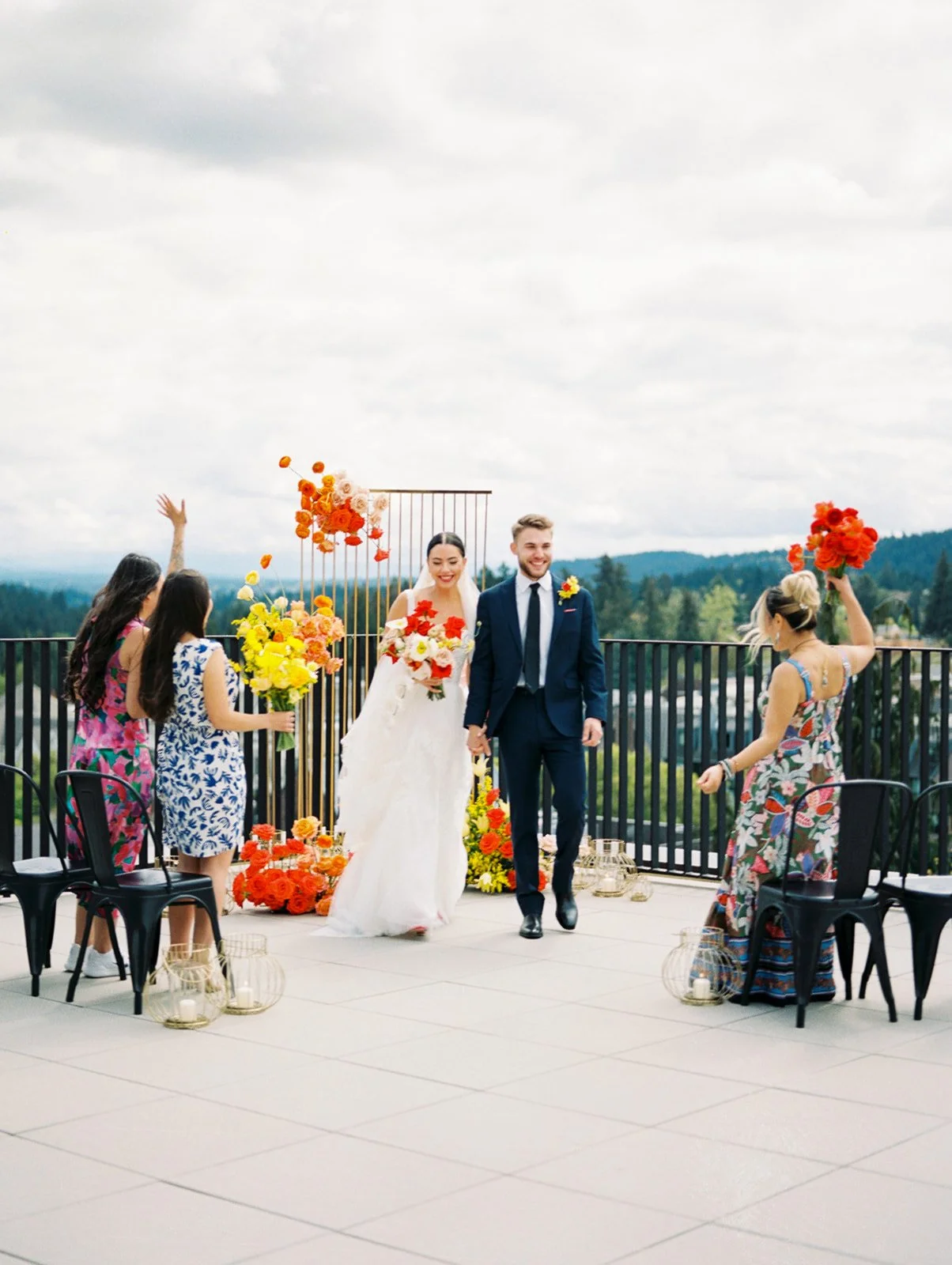 Newlyweds walking down aisle smiling as guests celebrate during rooftop wedding ceremony
