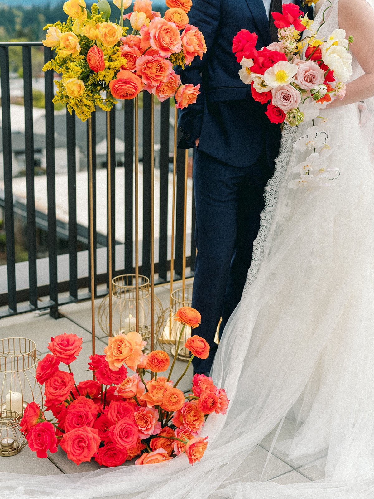 Colorful ceremony florals with bride’s gown and groom’s suit visible in modern rooftop setting