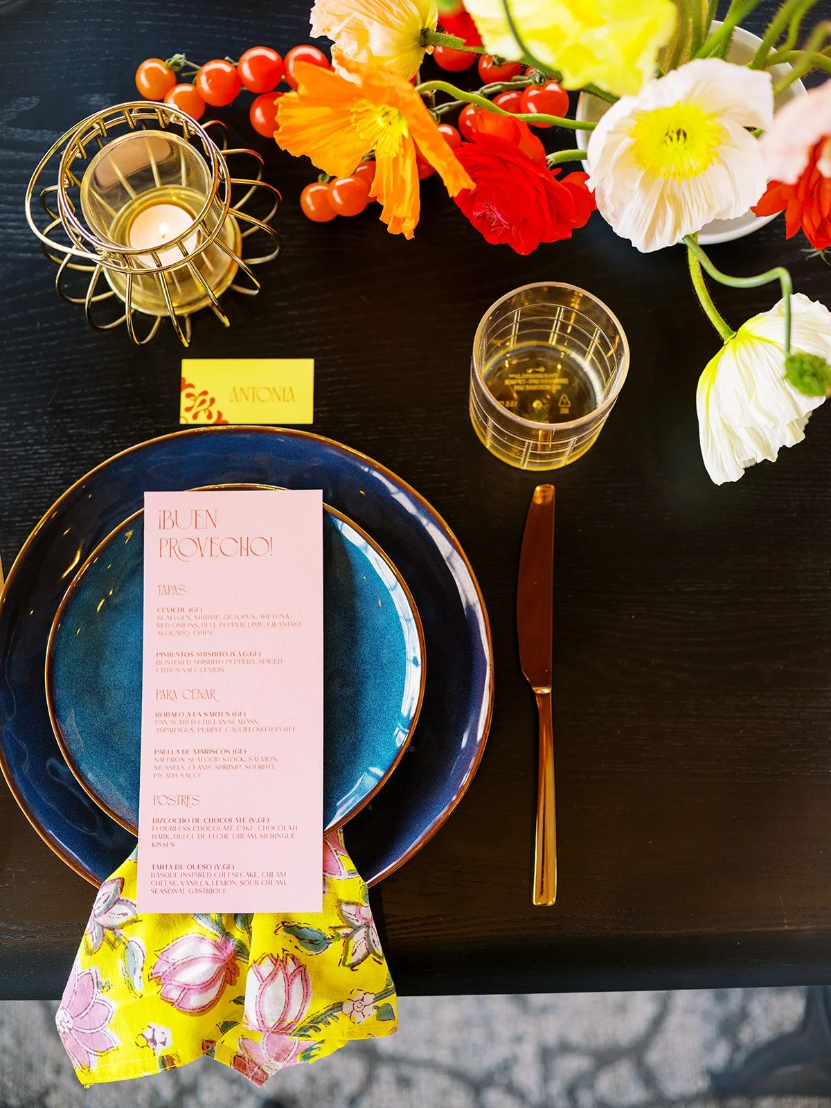 Wedding place setting with blue plate, floral napkin, printed menu, and colorful blooms on dark table