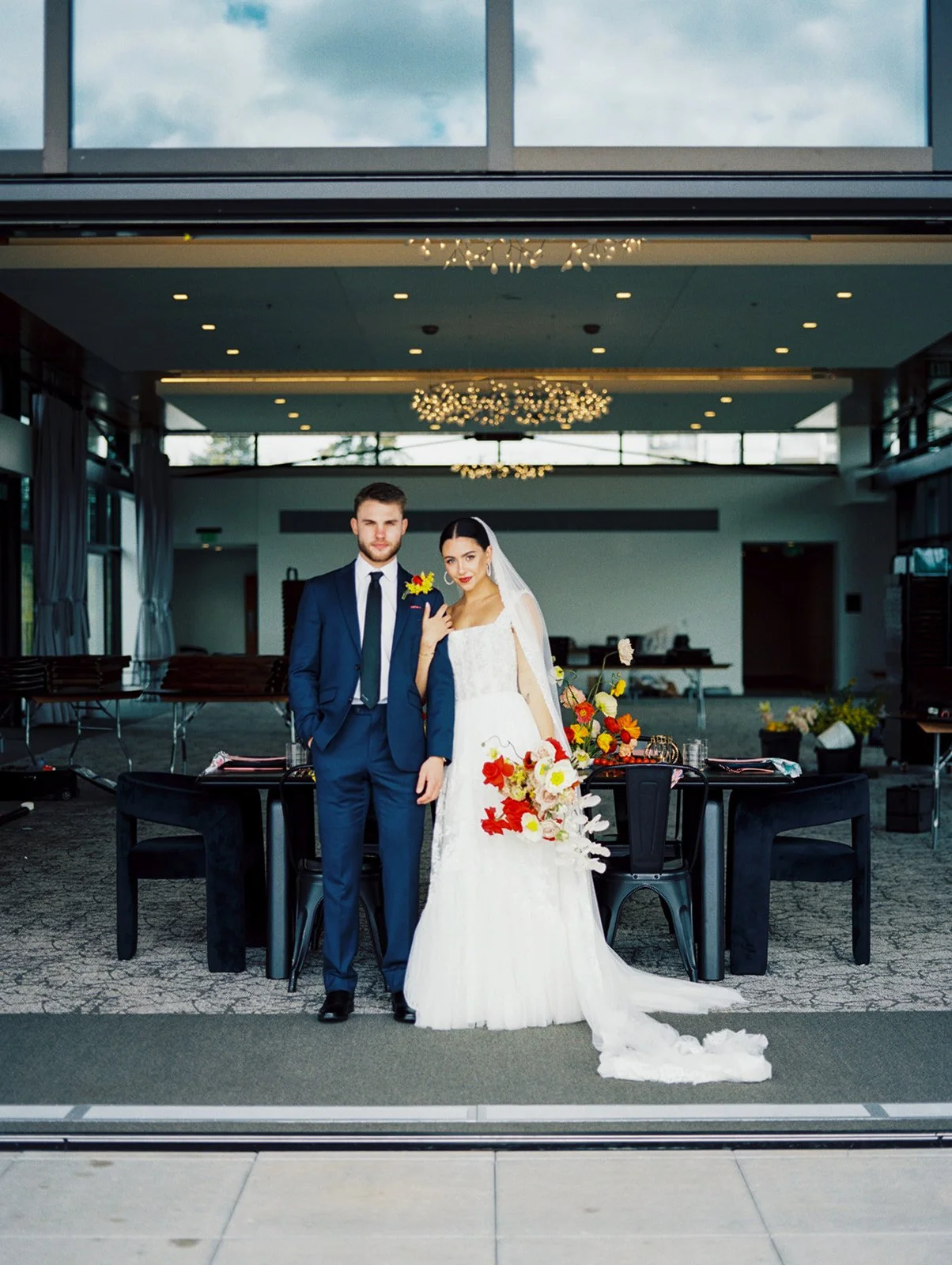 Bride and groom posing together at reception space with long table and floral arrangements