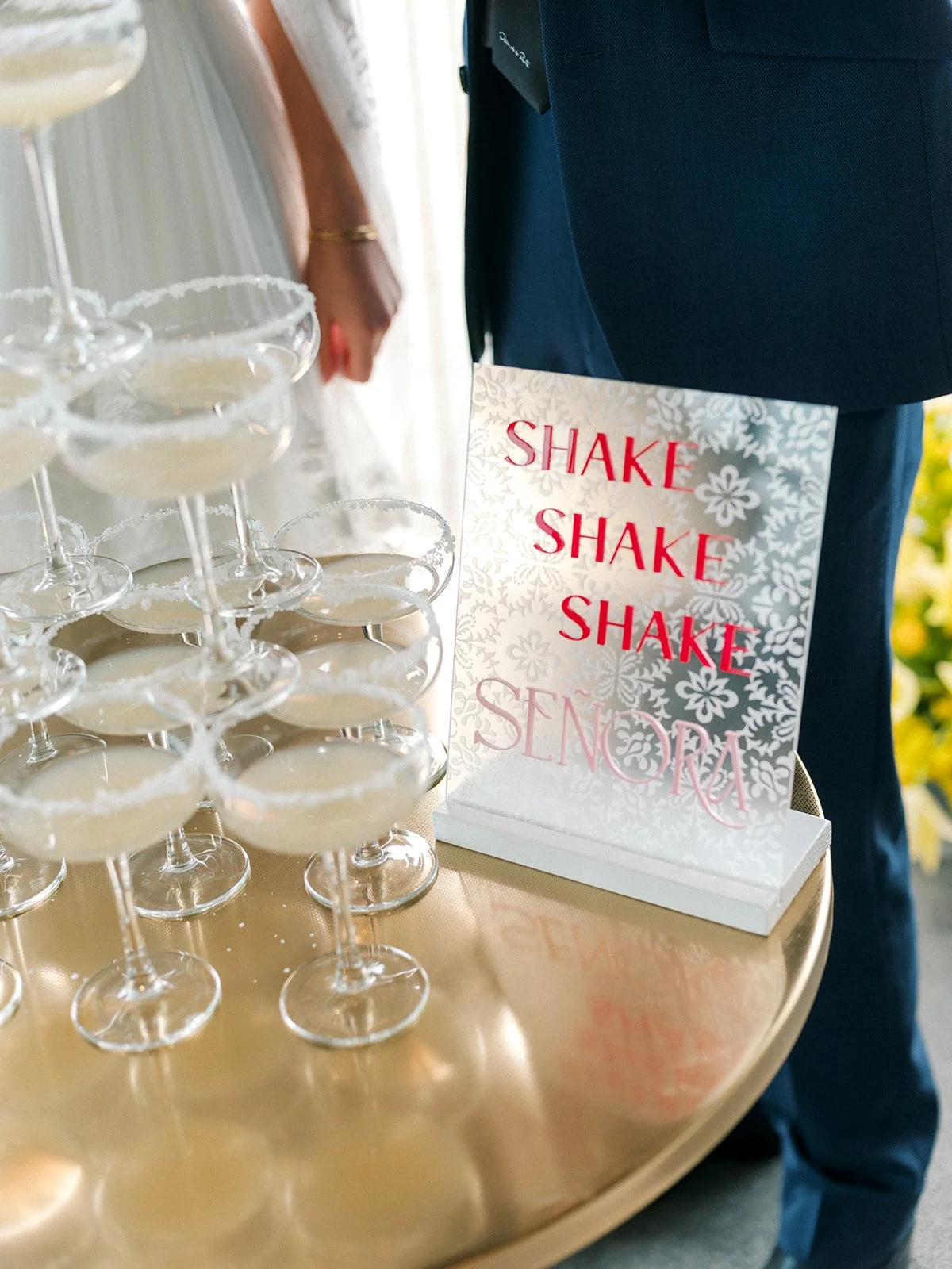 Margarita tower with coupe glasses and sign reading “shake shake shake señora” on gold table