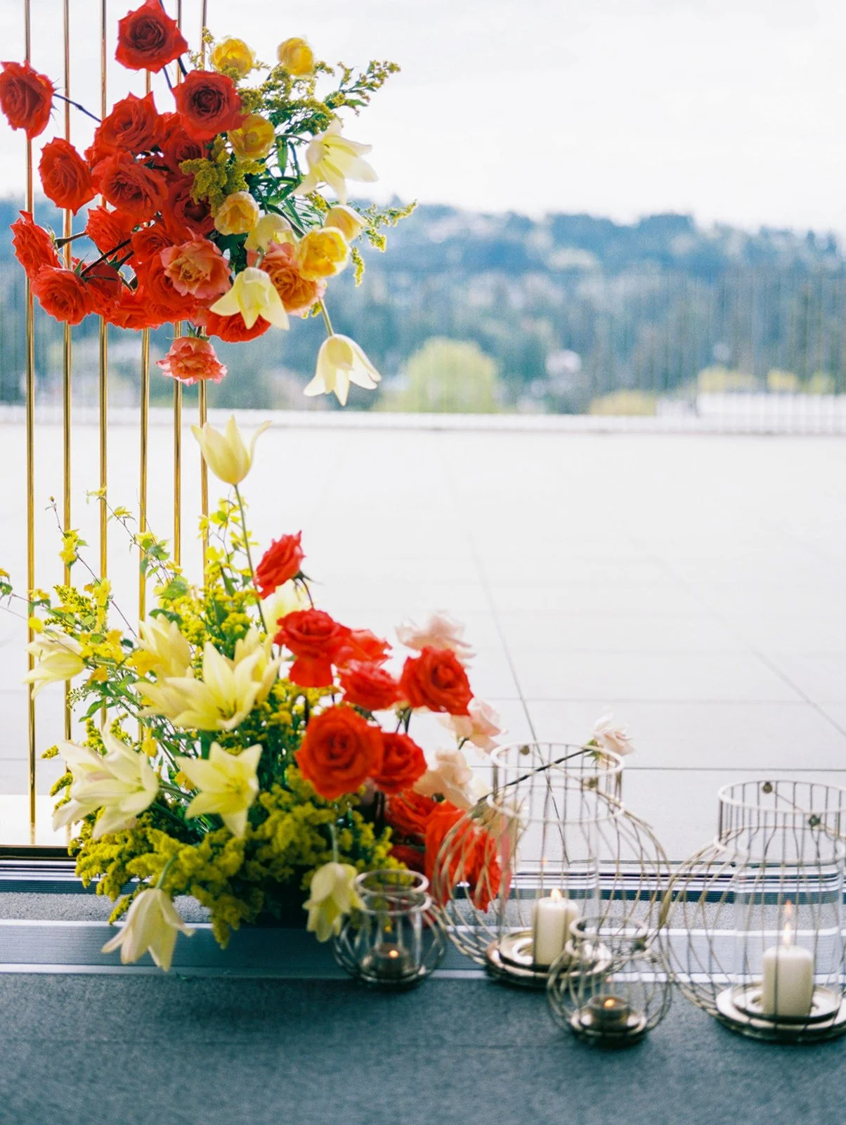 Colorful ceremony florals with red and yellow blooms and glass candle holders on rooftop wedding terrace