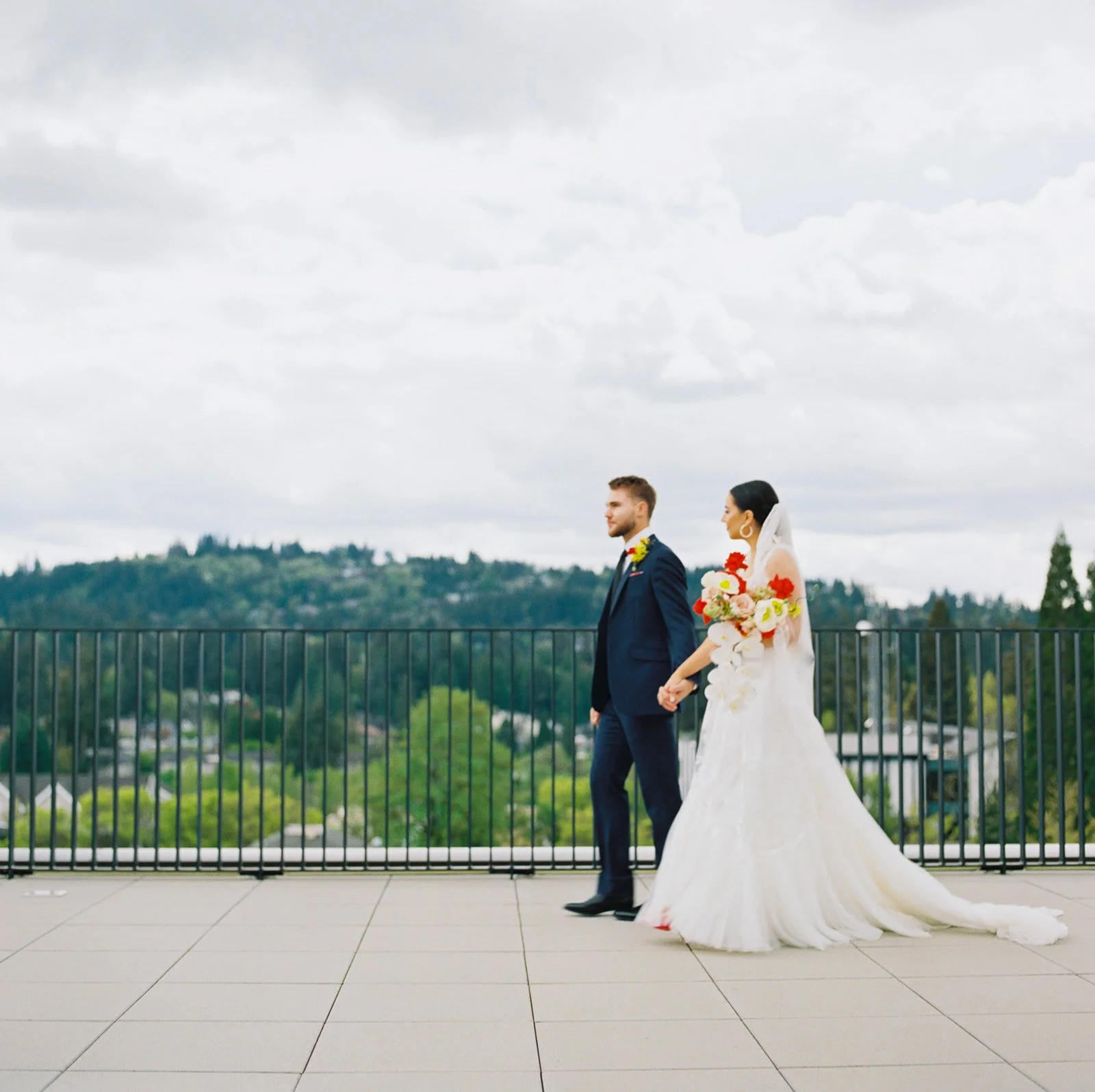 Bride and groom walking hand in hand along rooftop terrace with scenic Oregon landscape in background