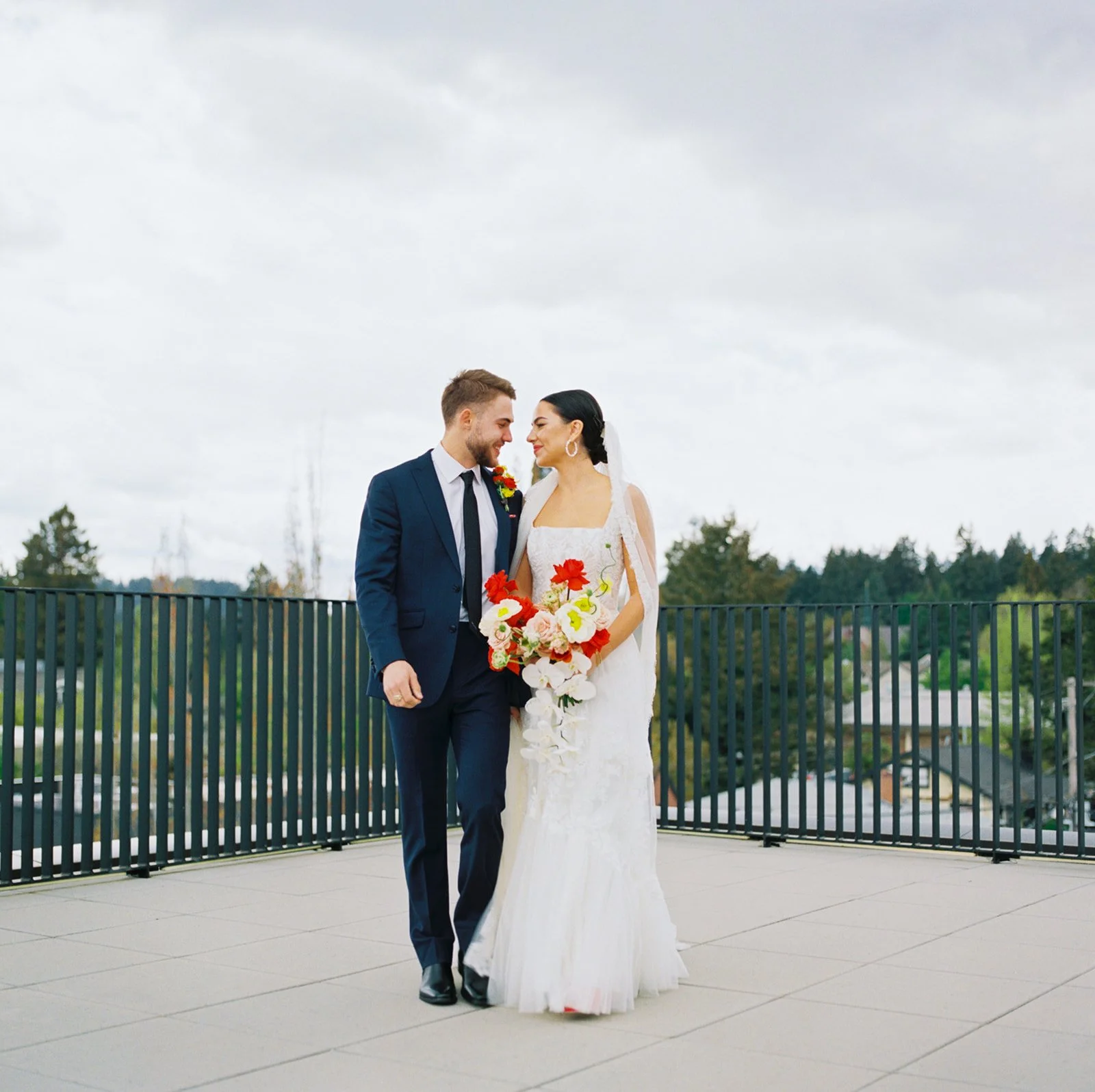 Bride and groom walking together on rooftop, holding bouquet and looking at each other