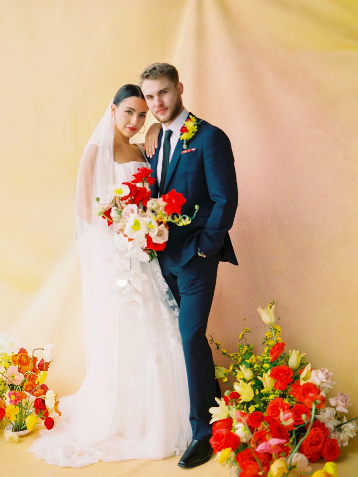 Bride and groom posing with colorful bouquet in front of gold backdrop and floral installations