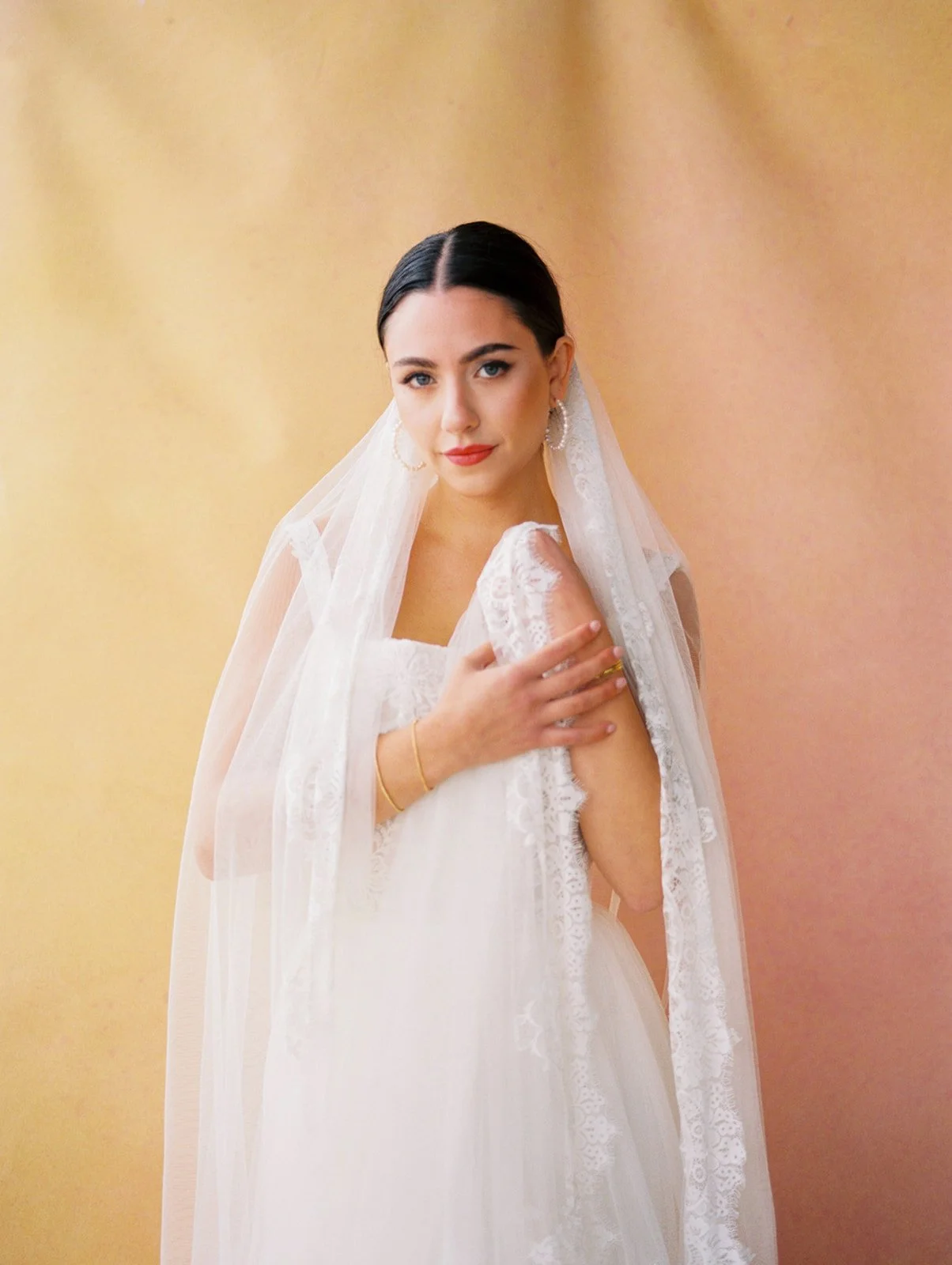 Bride portrait with lace veil and earrings against warm gold backdrop at modern wedding venue