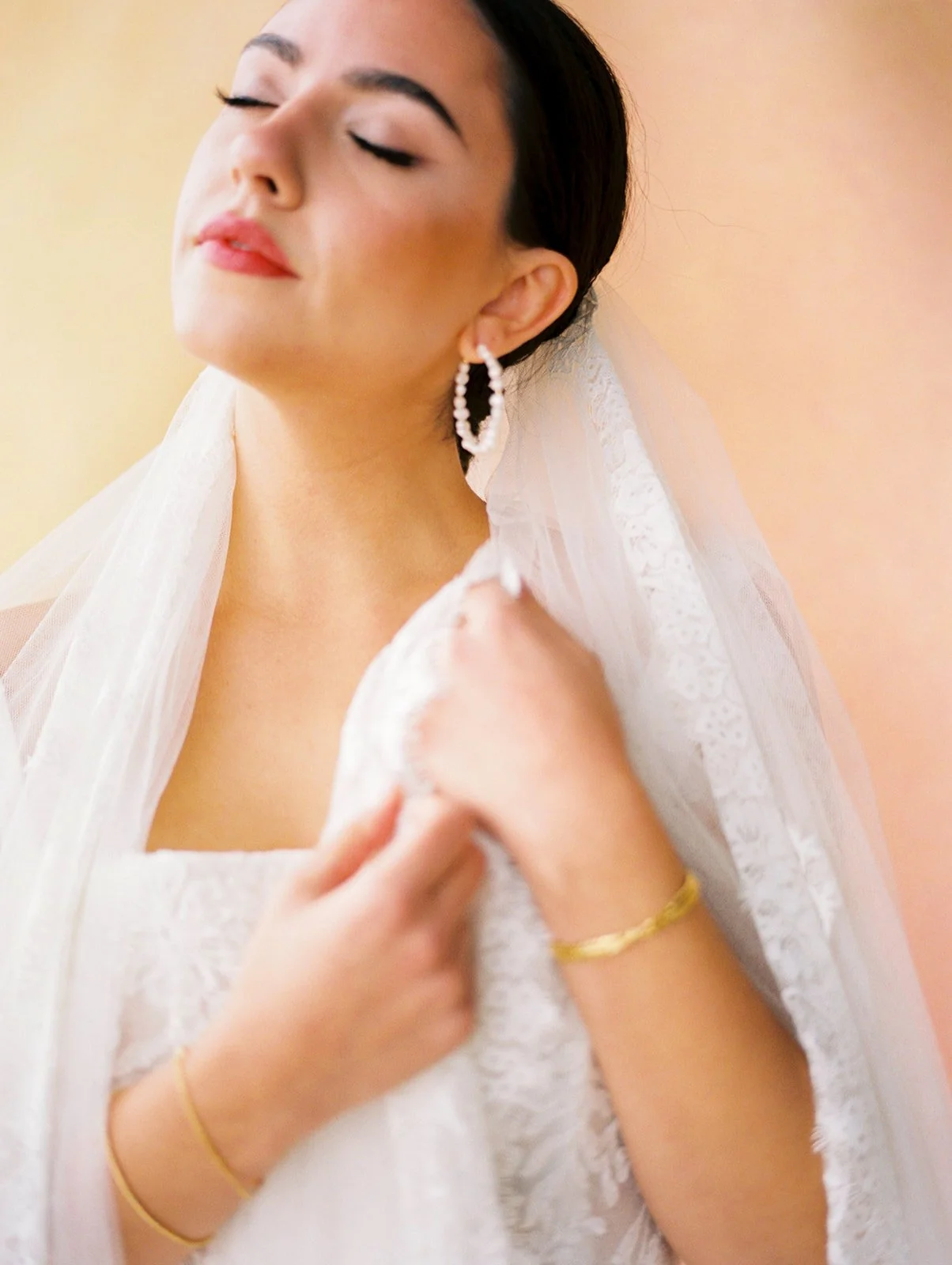 Close-up of bride with lace veil and hoop earrings against soft gold background