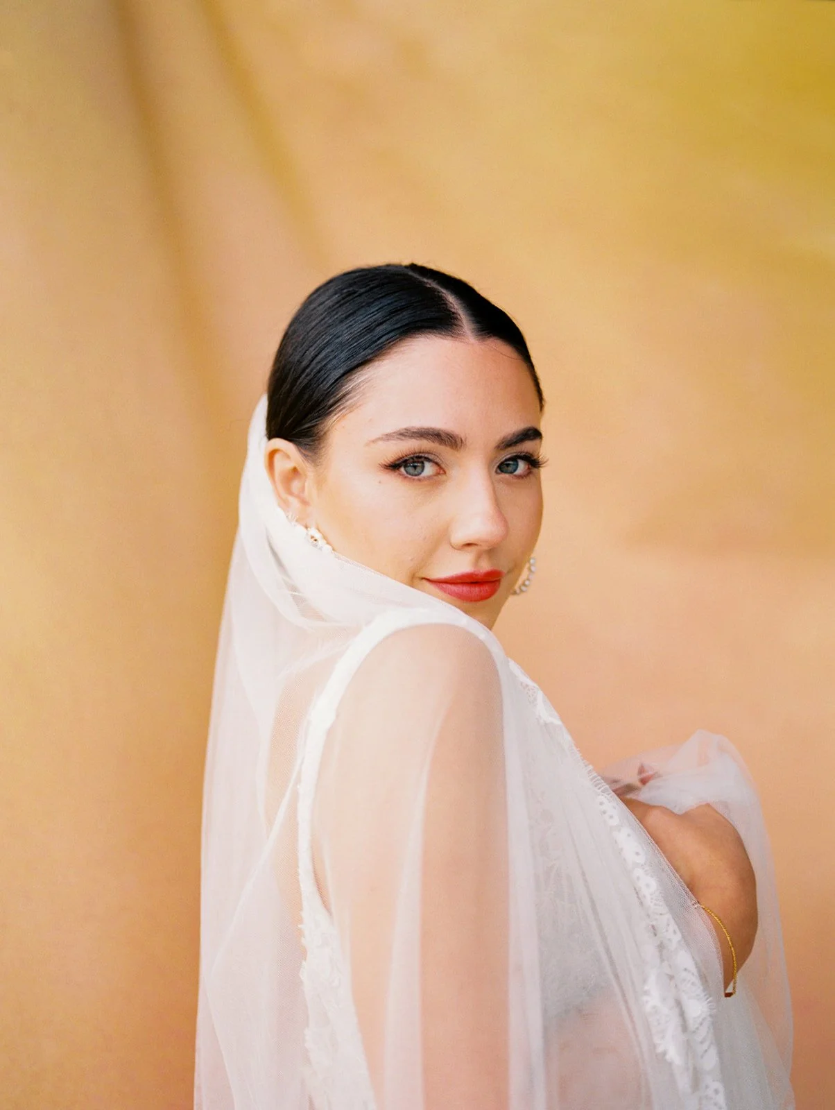 Close-up portrait of bride in veil looking over shoulder against warm golden backdrop