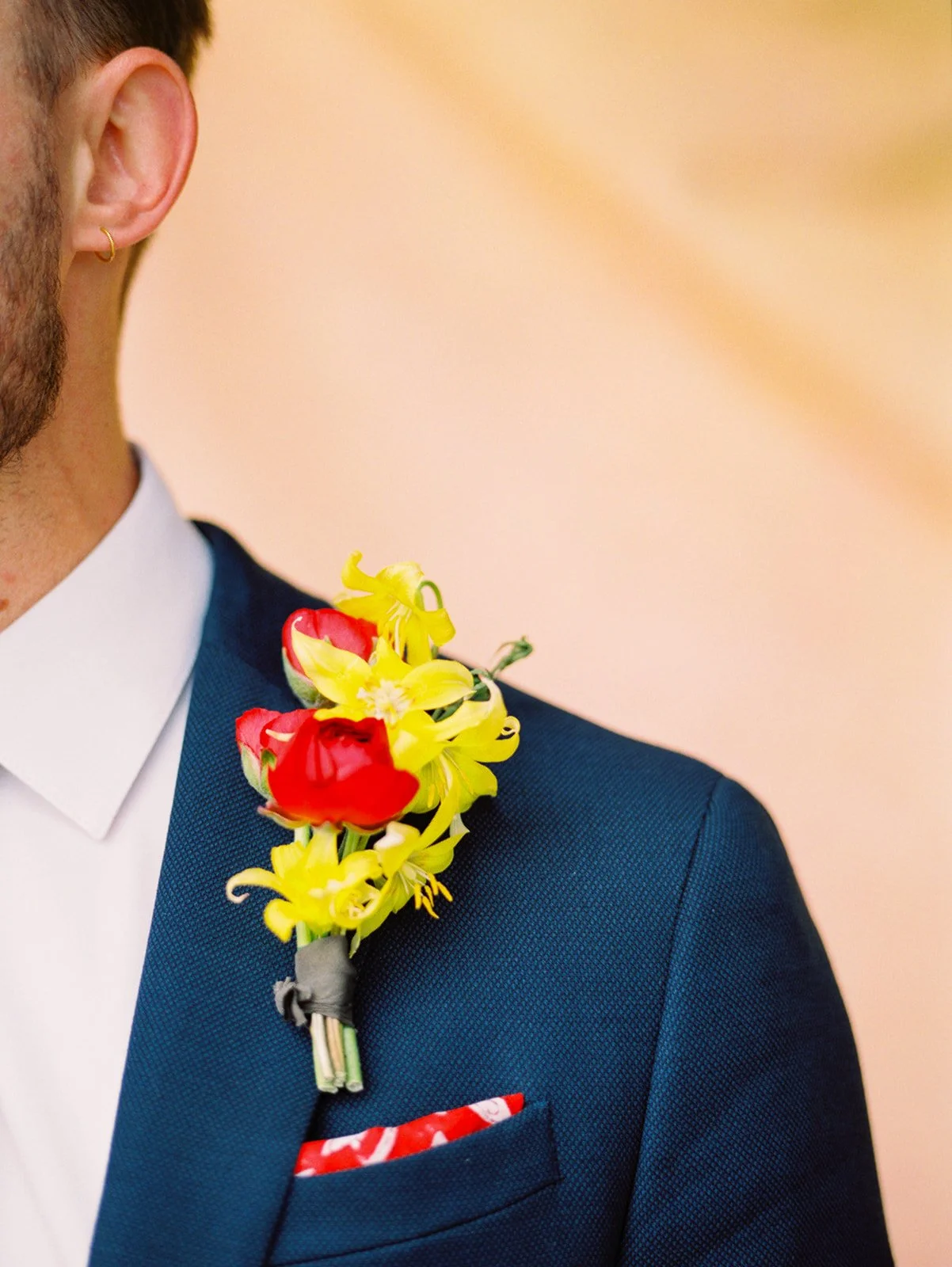 Close-up of groom’s navy suit with red and yellow boutonniere and patterned pocket square