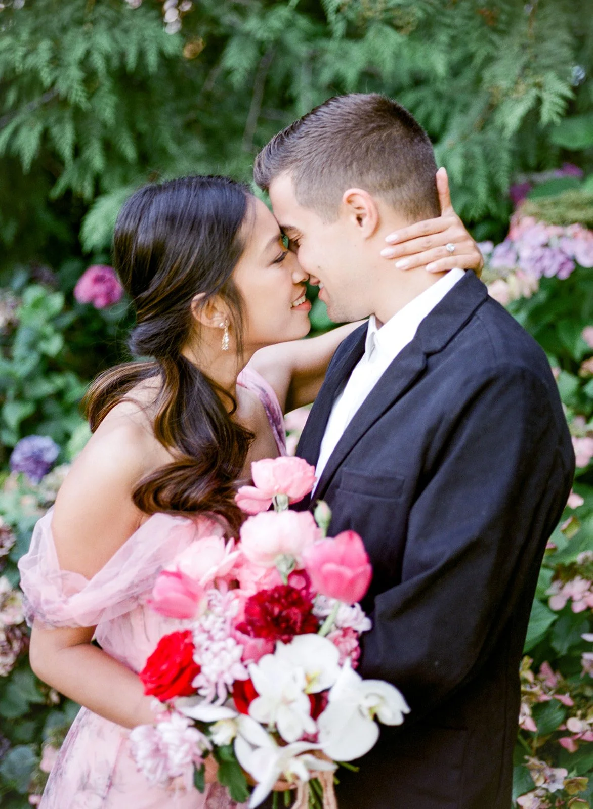 Couple leaning in for a kiss with colorful bouquet and garden backdrop in Cathedral Park.
