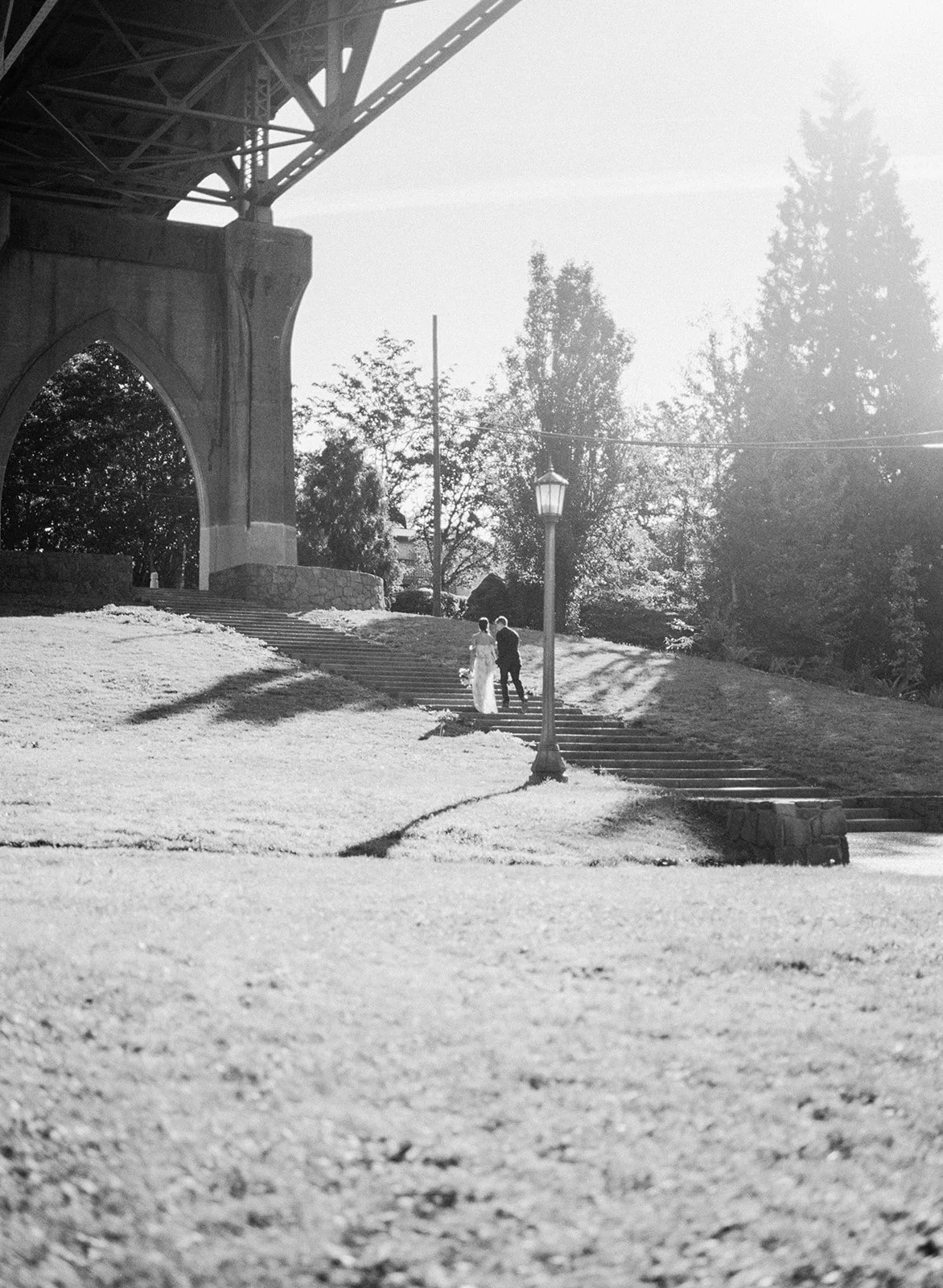 Couple walking up stone steps beneath bridge arches in Cathedral Park, black and white photo.