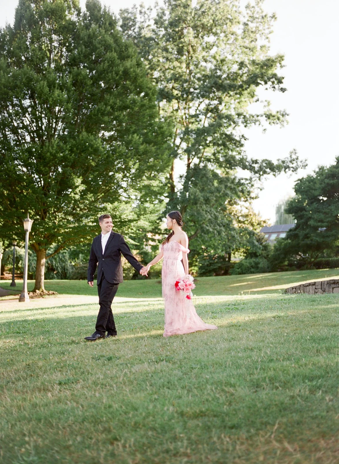 Couple holding hands and walking across grassy field in Cathedral Park at golden hour.
