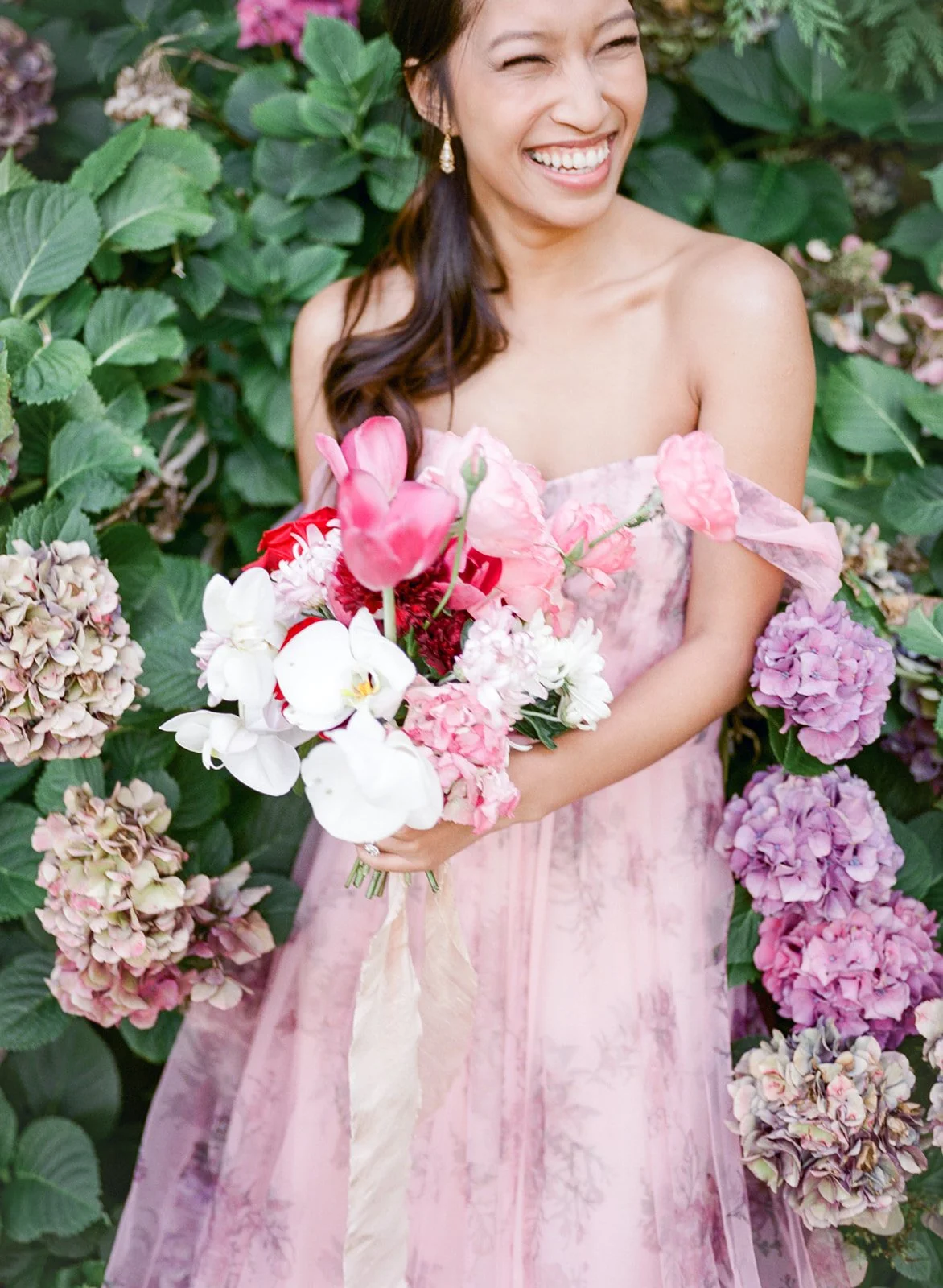 Bride laughing while holding bouquet among blooming hydrangeas in Cathedral Park.